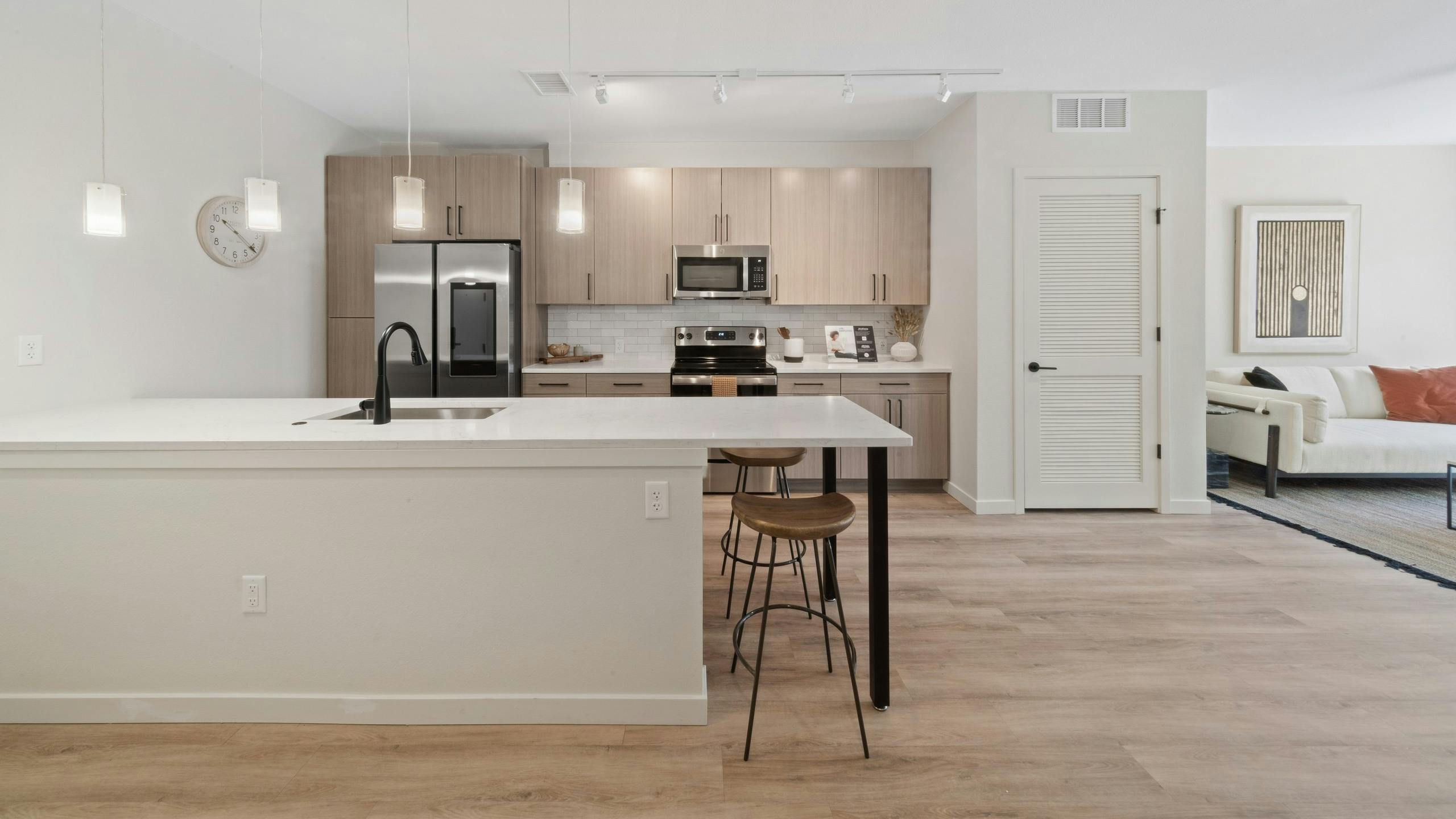 AMLI Broadway Park island kitchen featuring a stainless appliances and light wood grain cabinets over white tile backsplash