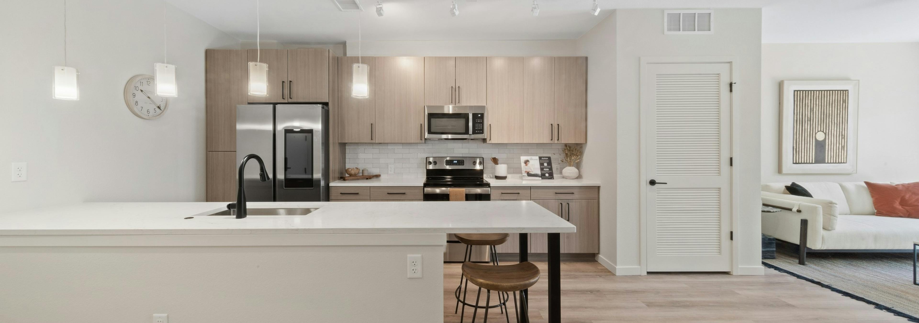 AMLI Broadway Park island kitchen featuring a stainless appliances and light wood grain cabinets over white tile backsplash 