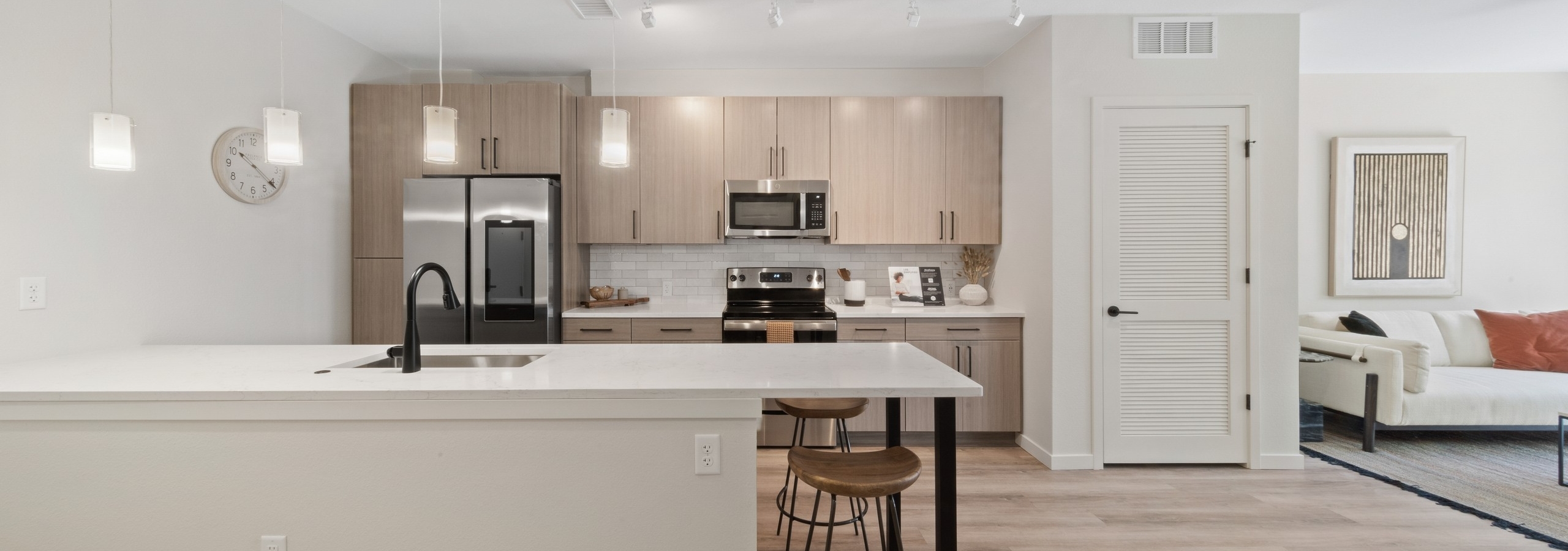 AMLI Broadway Park island kitchen featuring a stainless appliances and light wood grain cabinets over white tile backsplash