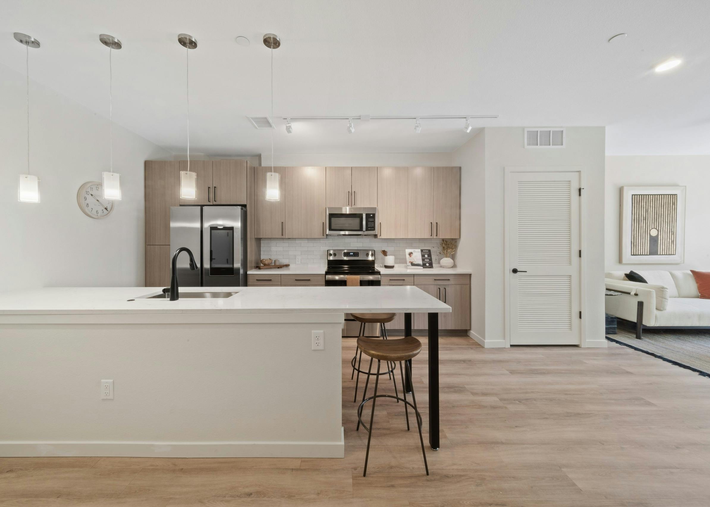 AMLI Broadway Park island kitchen featuring a stainless appliances and light wood grain cabinets over white tile backsplash