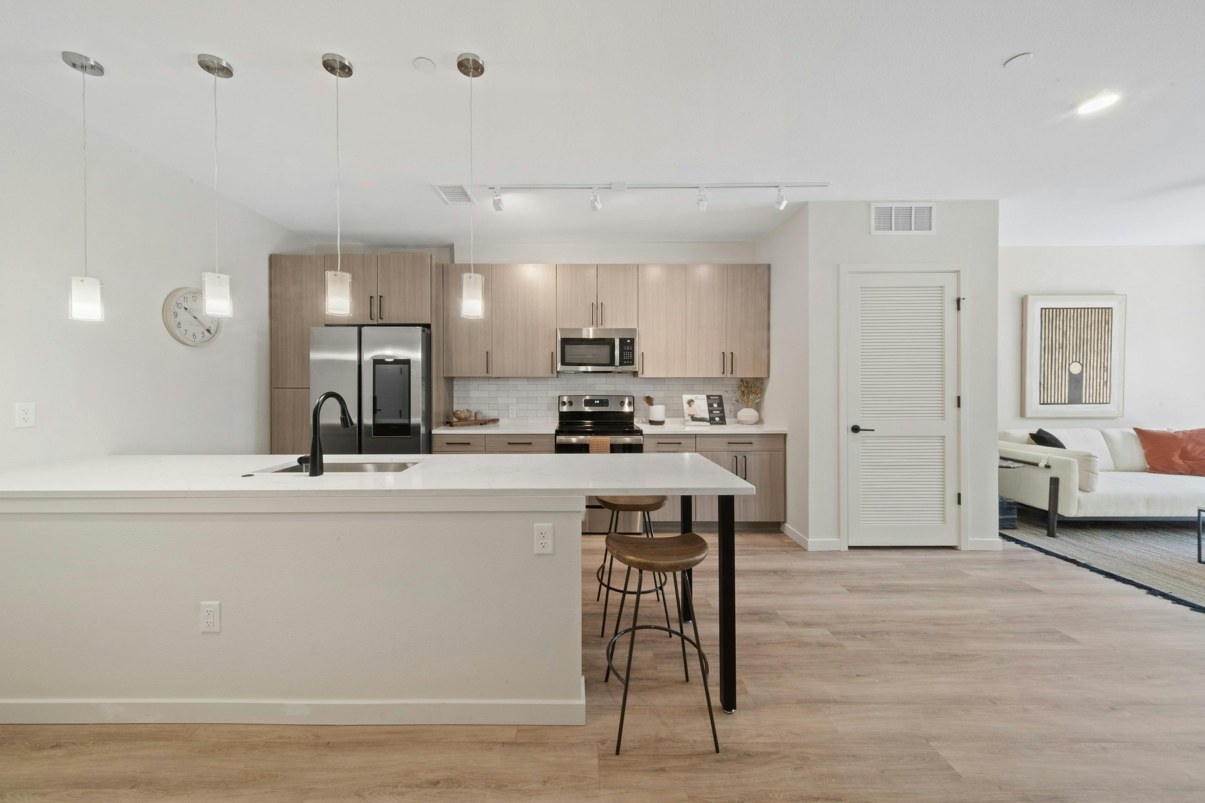 AMLI Broadway Park island kitchen featuring a stainless appliances and light wood grain cabinets over white tile backsplash 