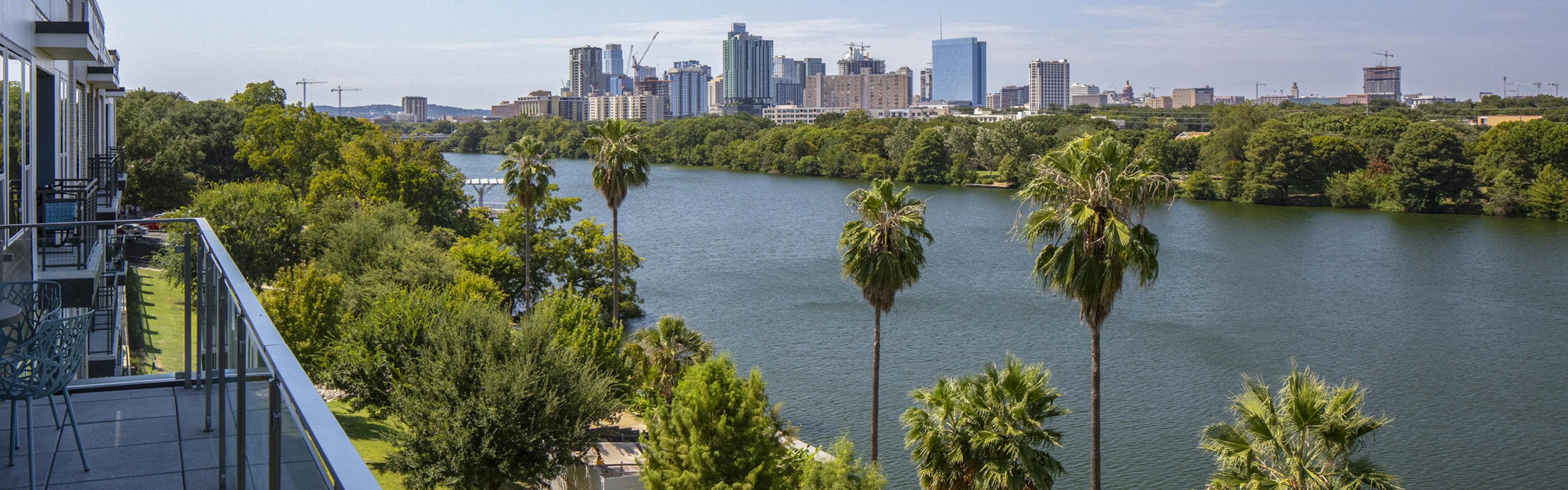 Daytime view of downtown Austin skyline and Lady Bird Lake from AMLI South Shore apartment building balcony with blue chairs 
