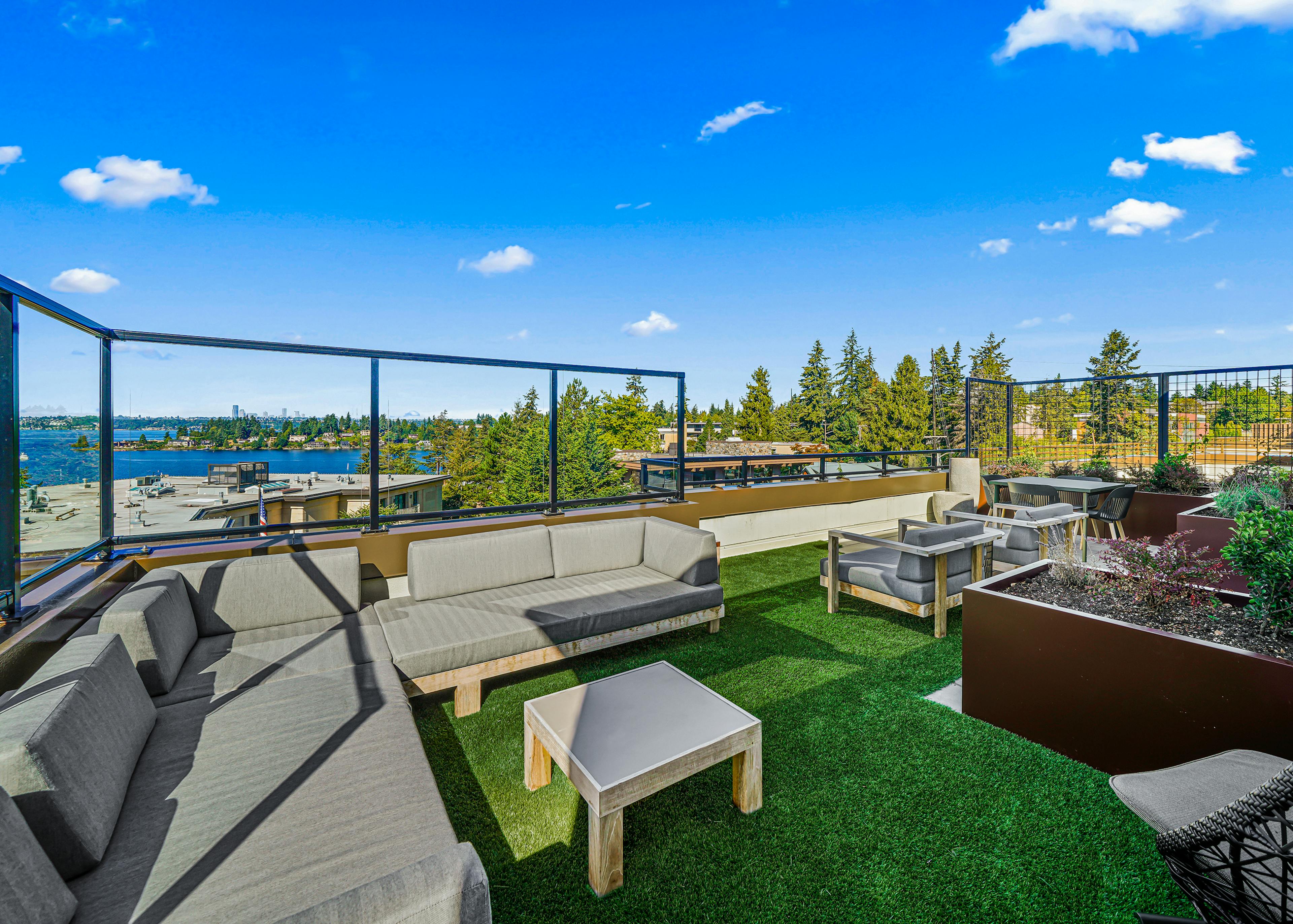 Exterior view of AMLI Bellevue Park rooftop deck with planter and gray couch on green turf and view of Lake Washington