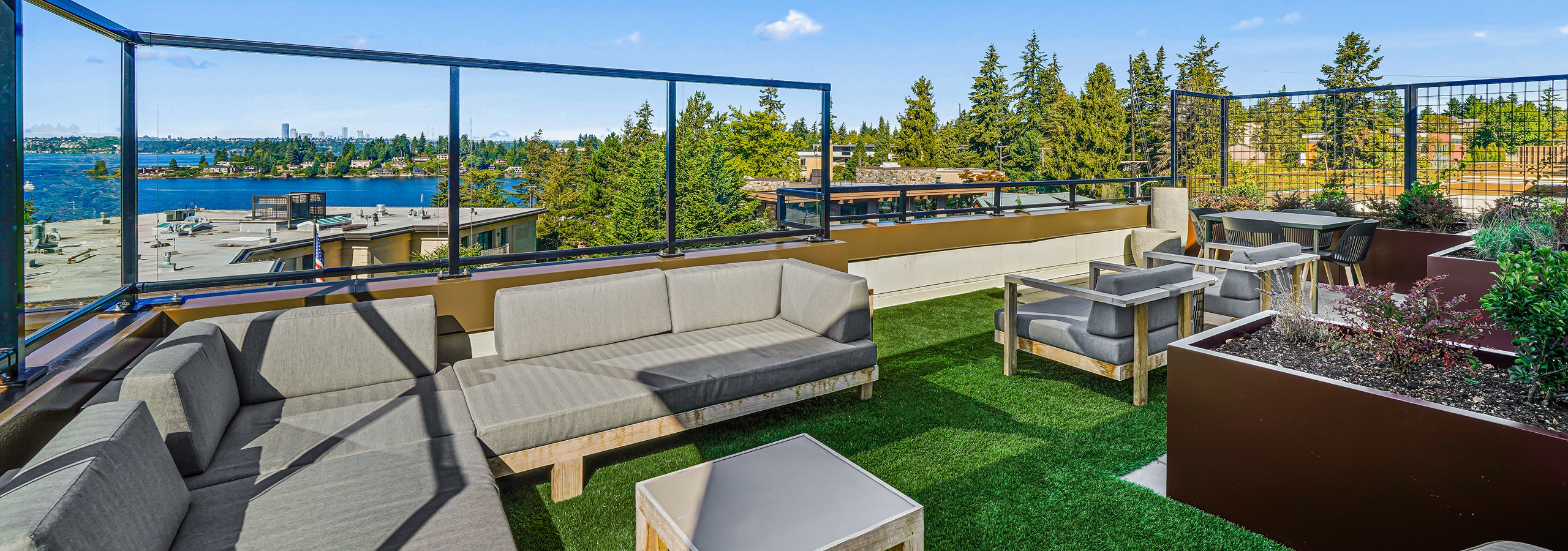 Exterior view of AMLI Bellevue Park rooftop deck with planter and gray couch on green turf and view of Lake Washington