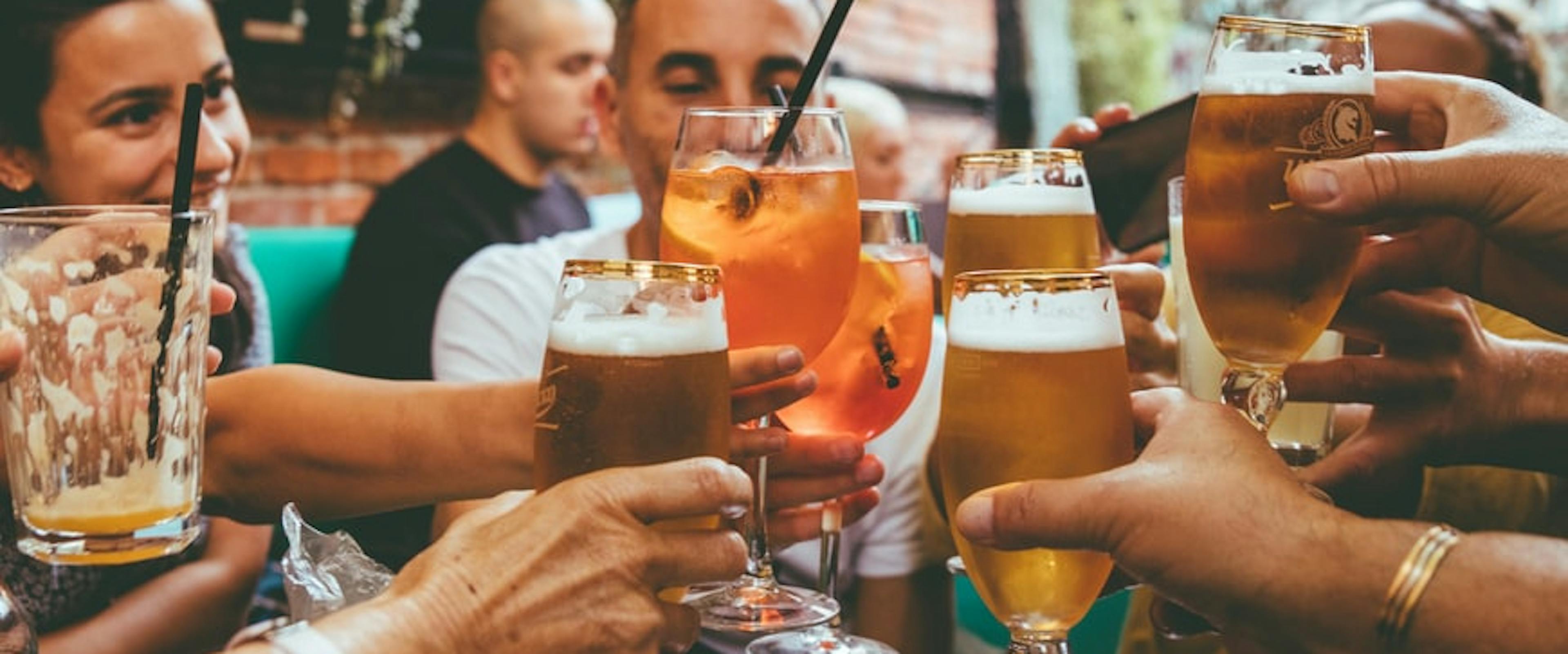 A group of people clinking beer glasses over brewery picnic table