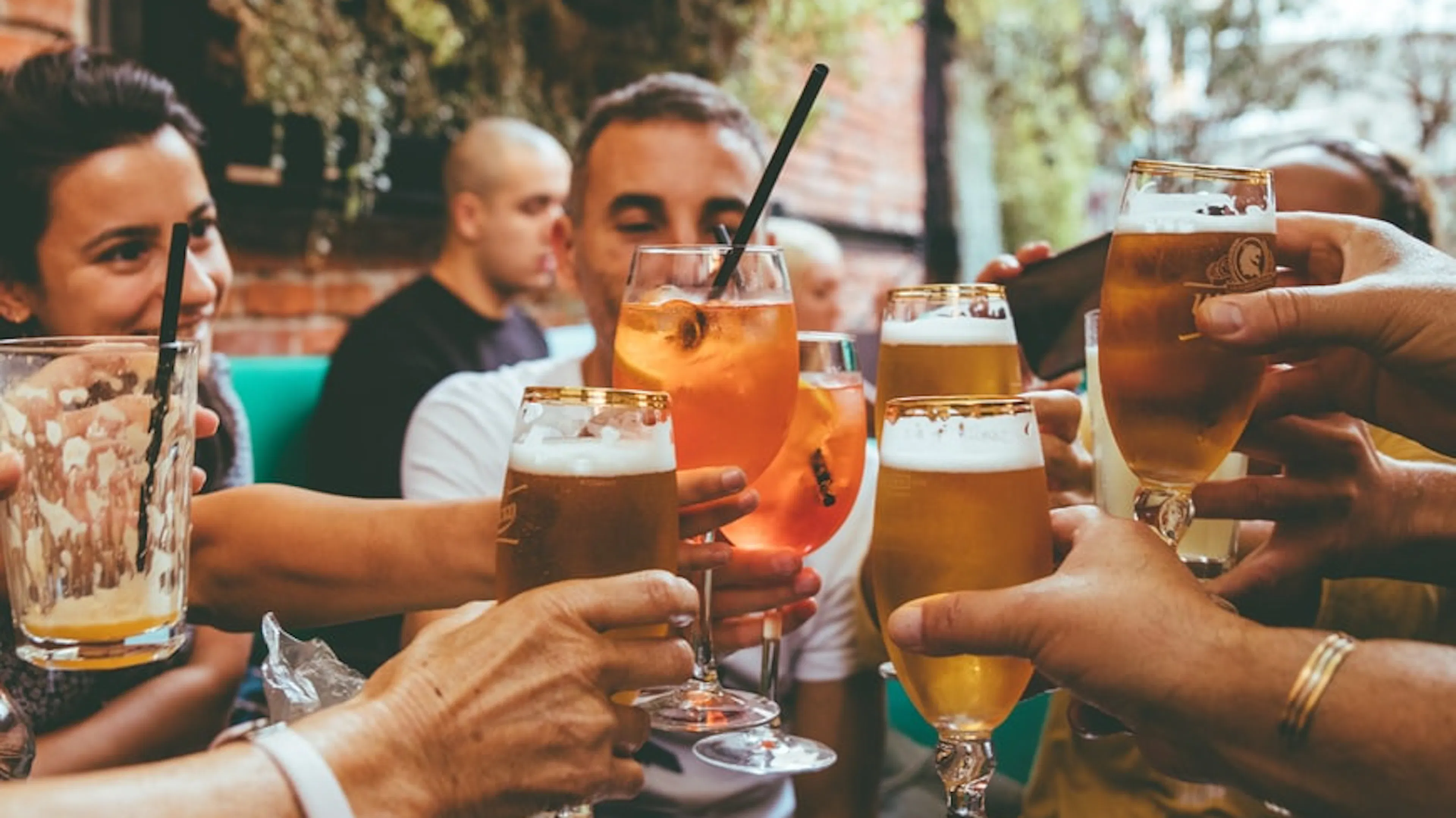 A group of people clinking beer glasses over brewery picnic table