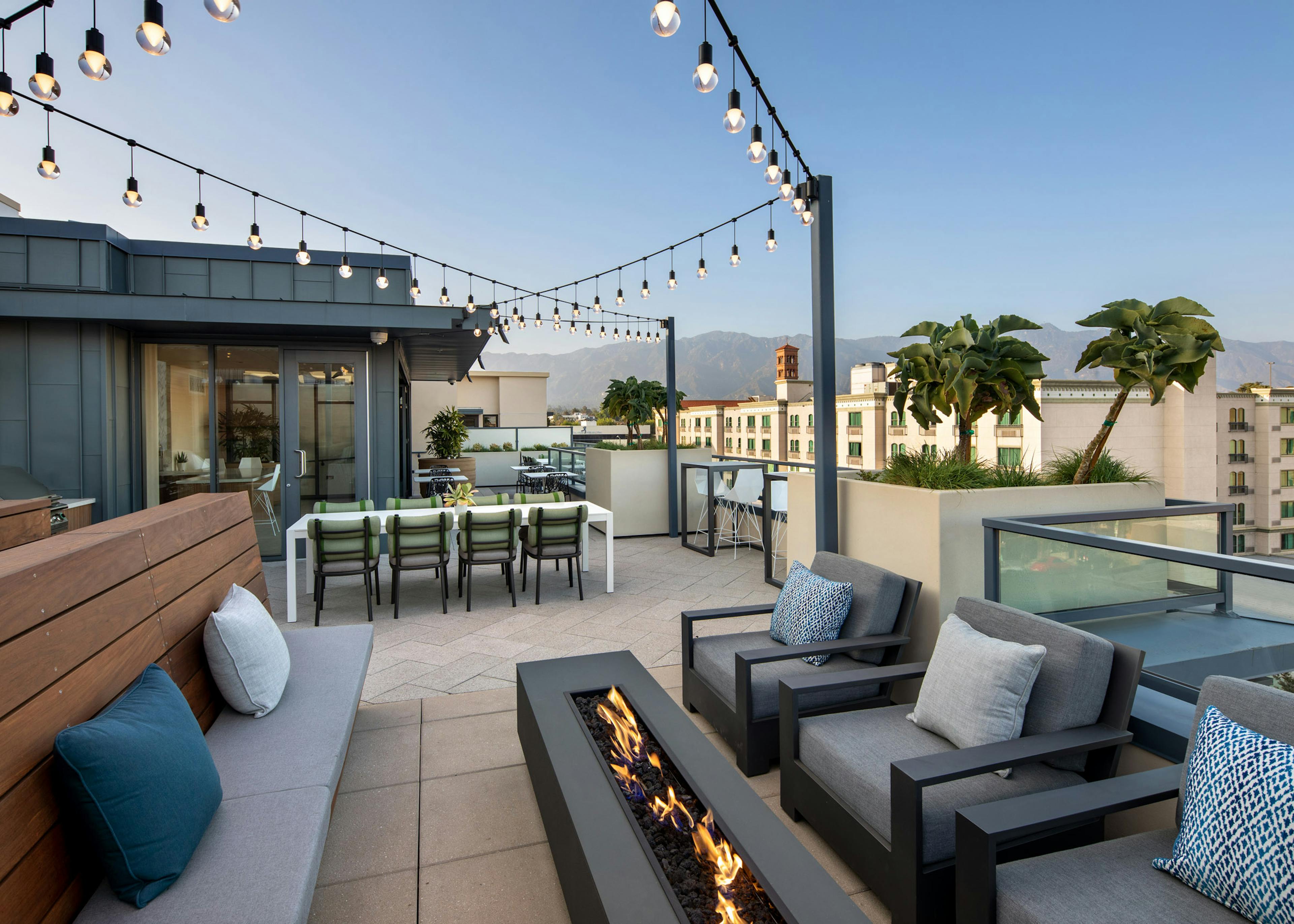 View of rooftop sky deck under a blue sky with firepit and hanging lights and various lounge seating at AMLI Old Pasadena