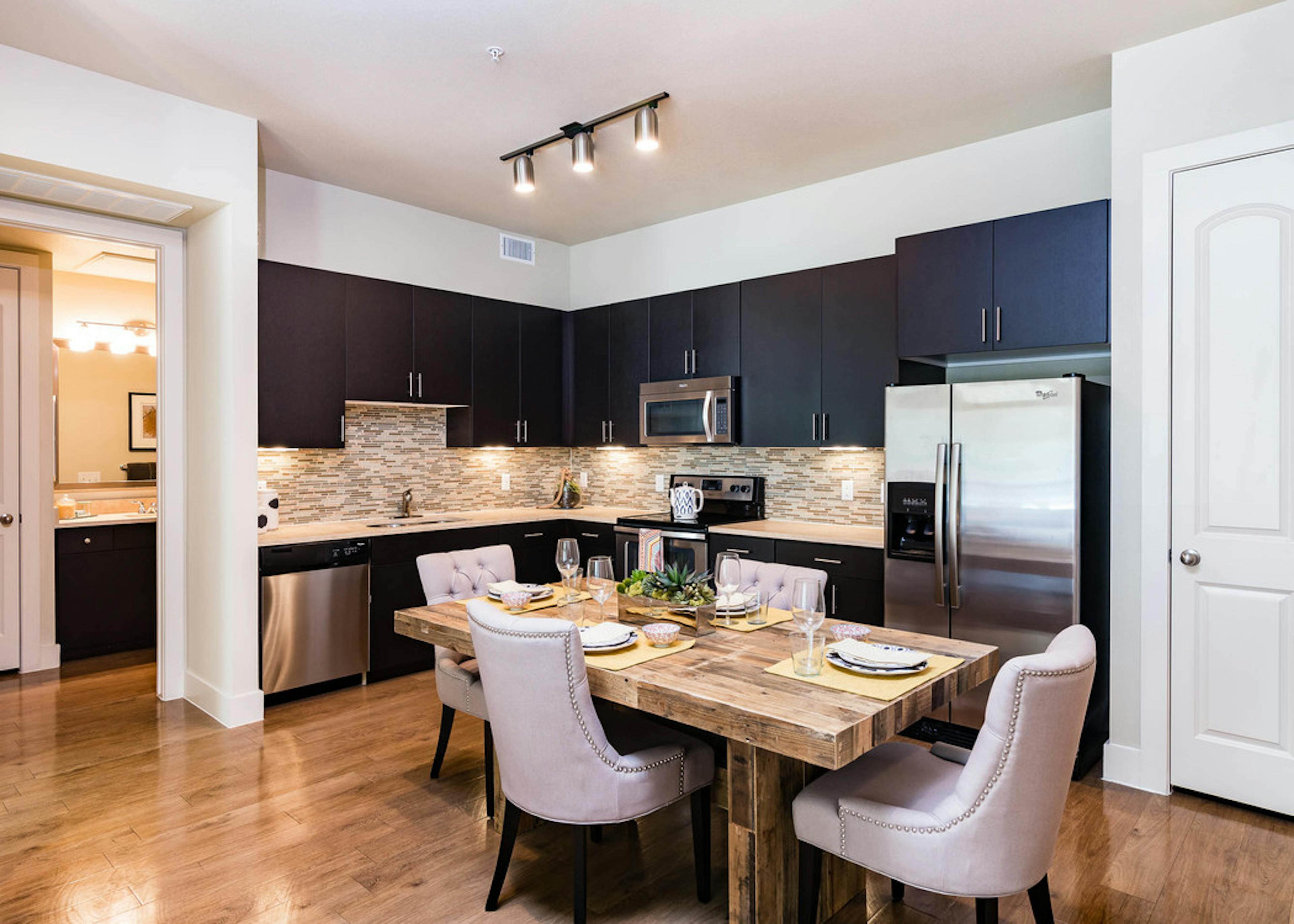 Interior view of AMLI RidgeGate dining area with table fully set and kitchen with dark cabinets and mosaic tile backsplash