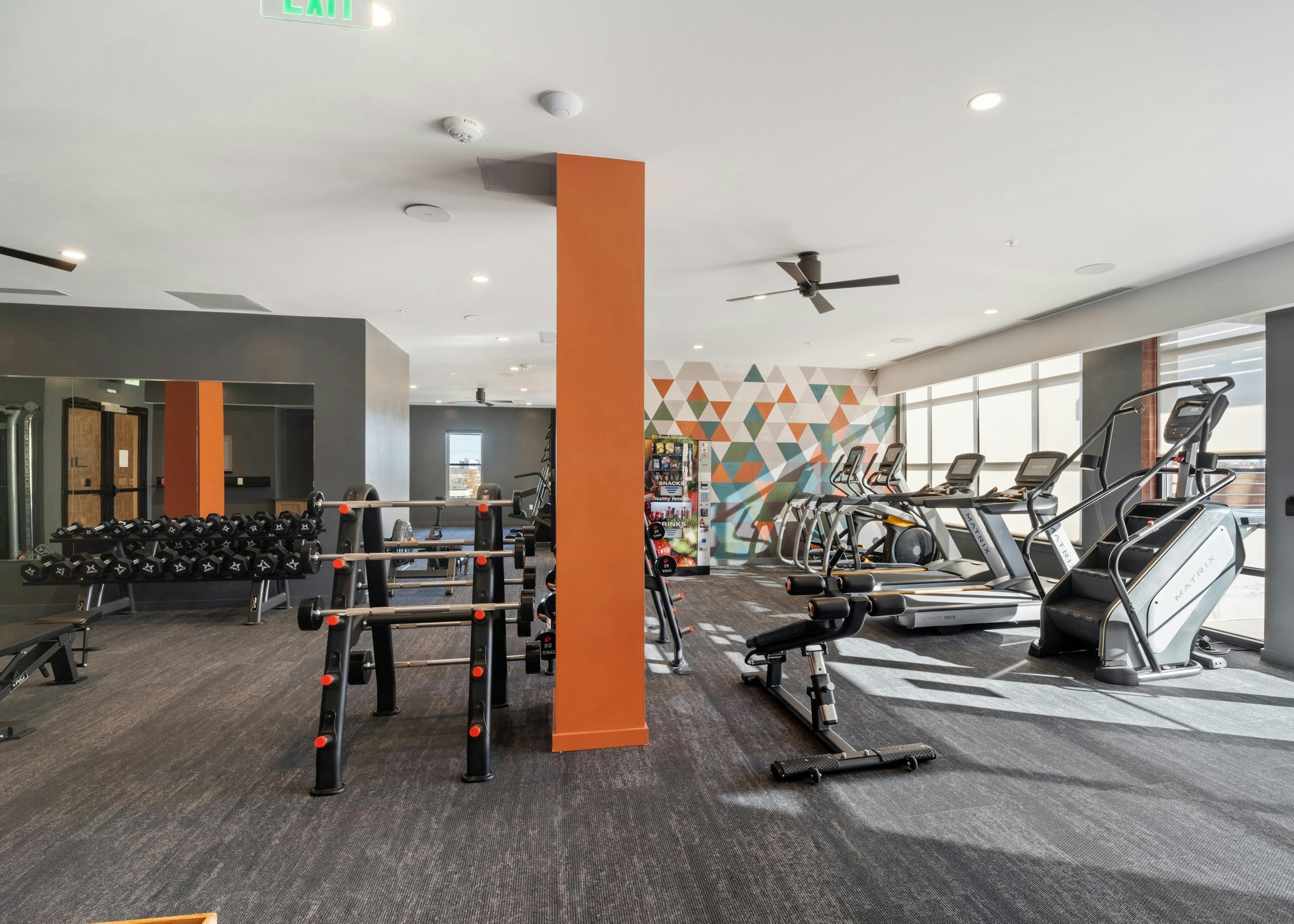 AMLI at Uptown fitness center with grey flooring featuring bright orange pillars and a wall of vibrant geometric artwork
