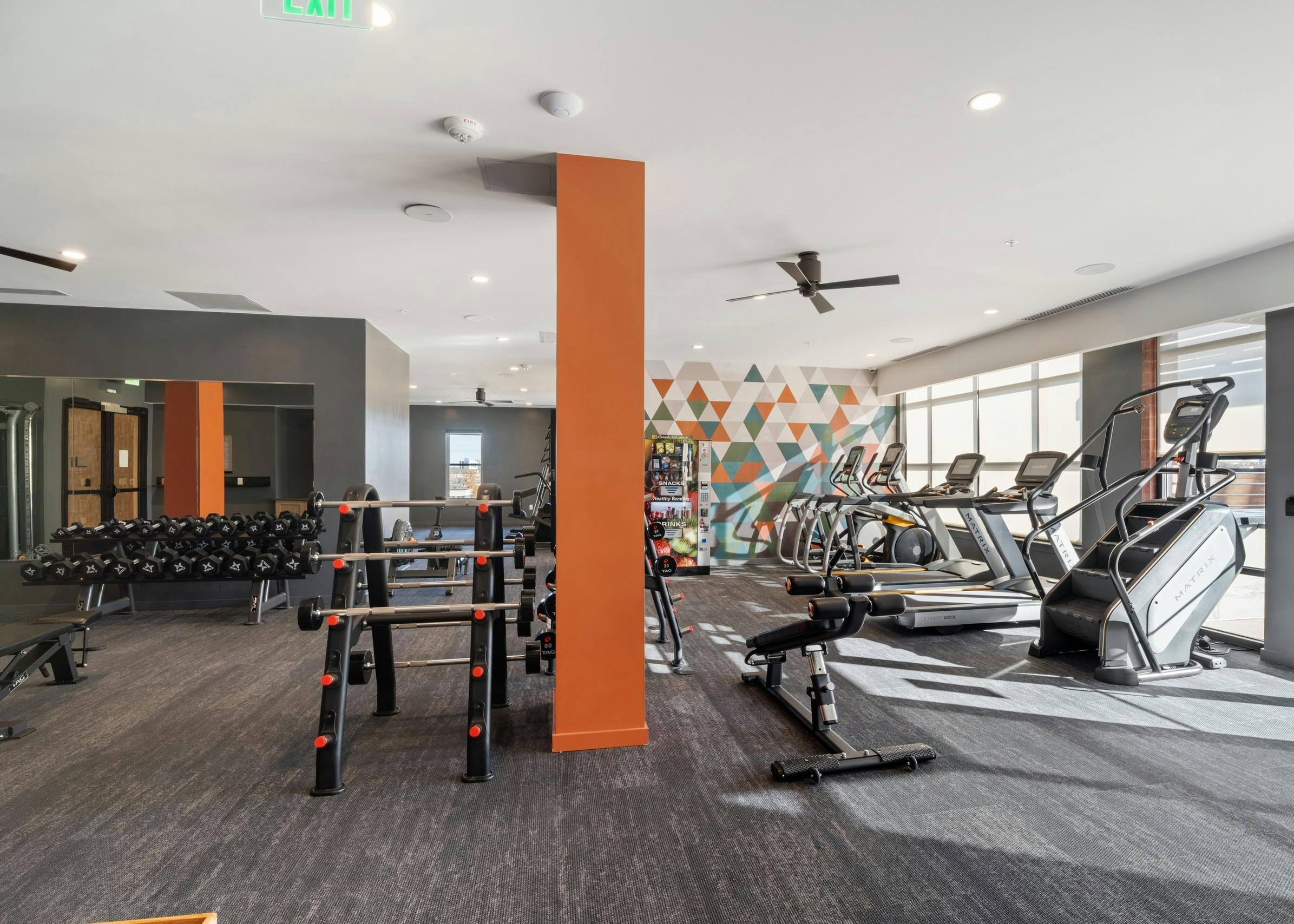 AMLI at Uptown fitness center with grey flooring featuring bright orange pillars and a wall of vibrant geometric artwork