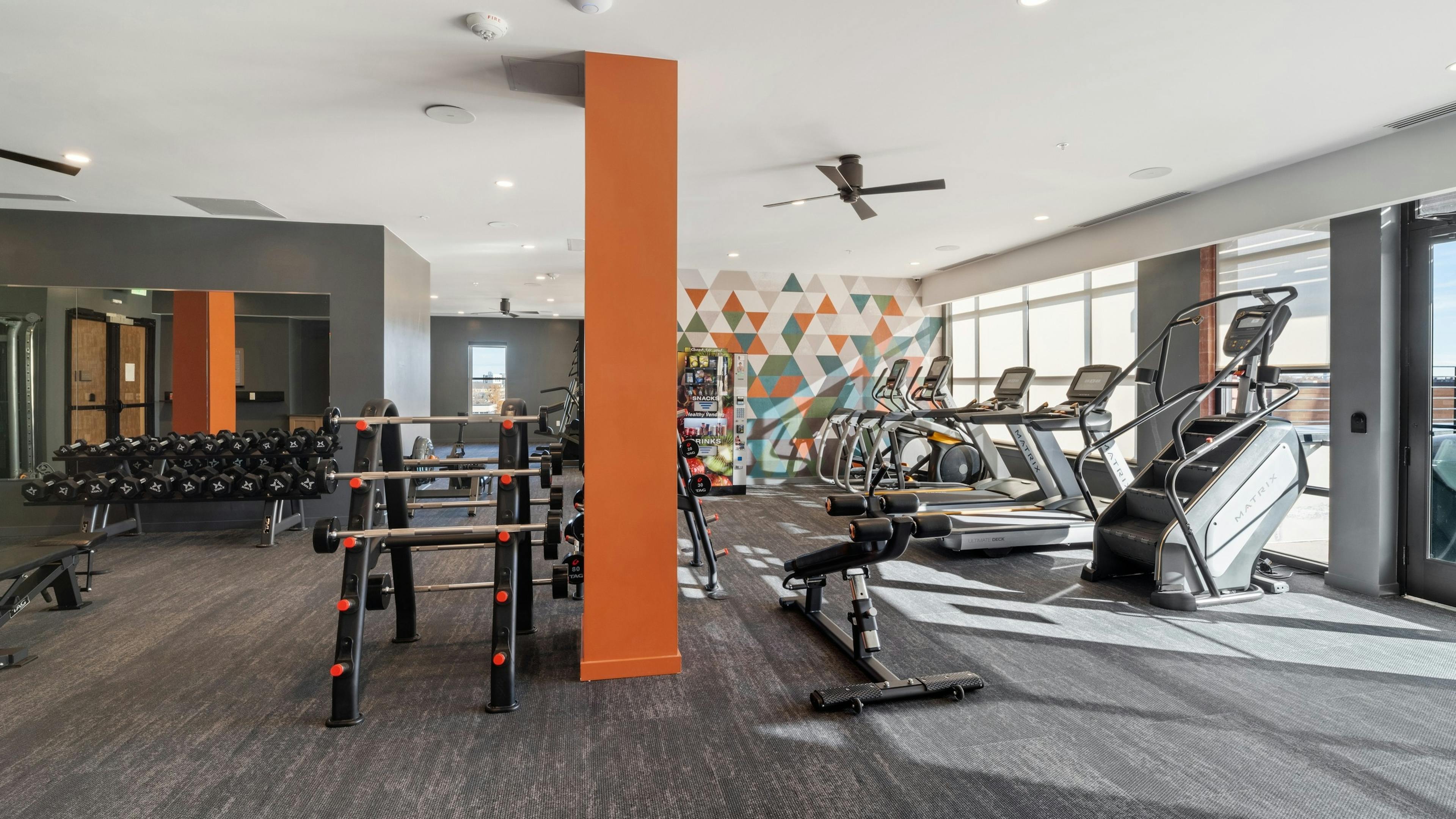 AMLI at Uptown fitness center with grey flooring featuring bright orange pillars and a wall of vibrant geometric artwork