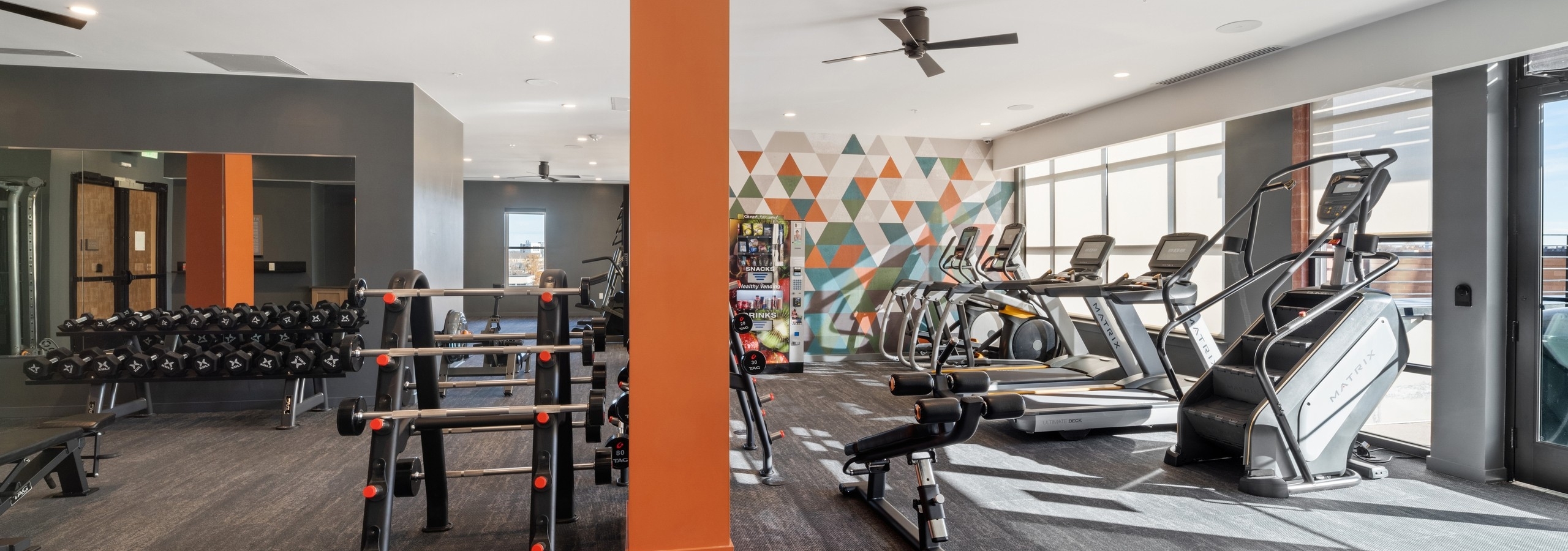 AMLI at Uptown fitness center with grey flooring featuring bright orange pillars and a wall of vibrant geometric artwork