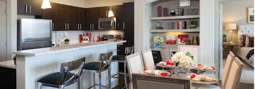 AMLI River Oaks apartment kitchen with stainless steel appliances and dark wood cabinetry and dining table with eight chairs