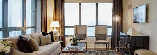 Penthouse living room at AMLI River North with a white leather sofa against one large window and two chairs against another