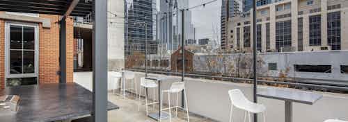 AMLI Downtown outdoor grill deck with white tall chairs and tables and string lights overlooking Austin skyscrapers and trees