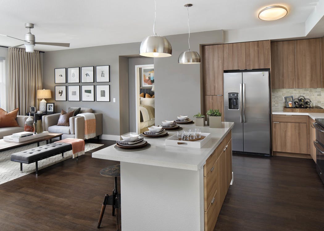 Interior of AMLI Uptown Orange apartment kitchen with quartz counters flowing into a furnished living room with ceiling fan
