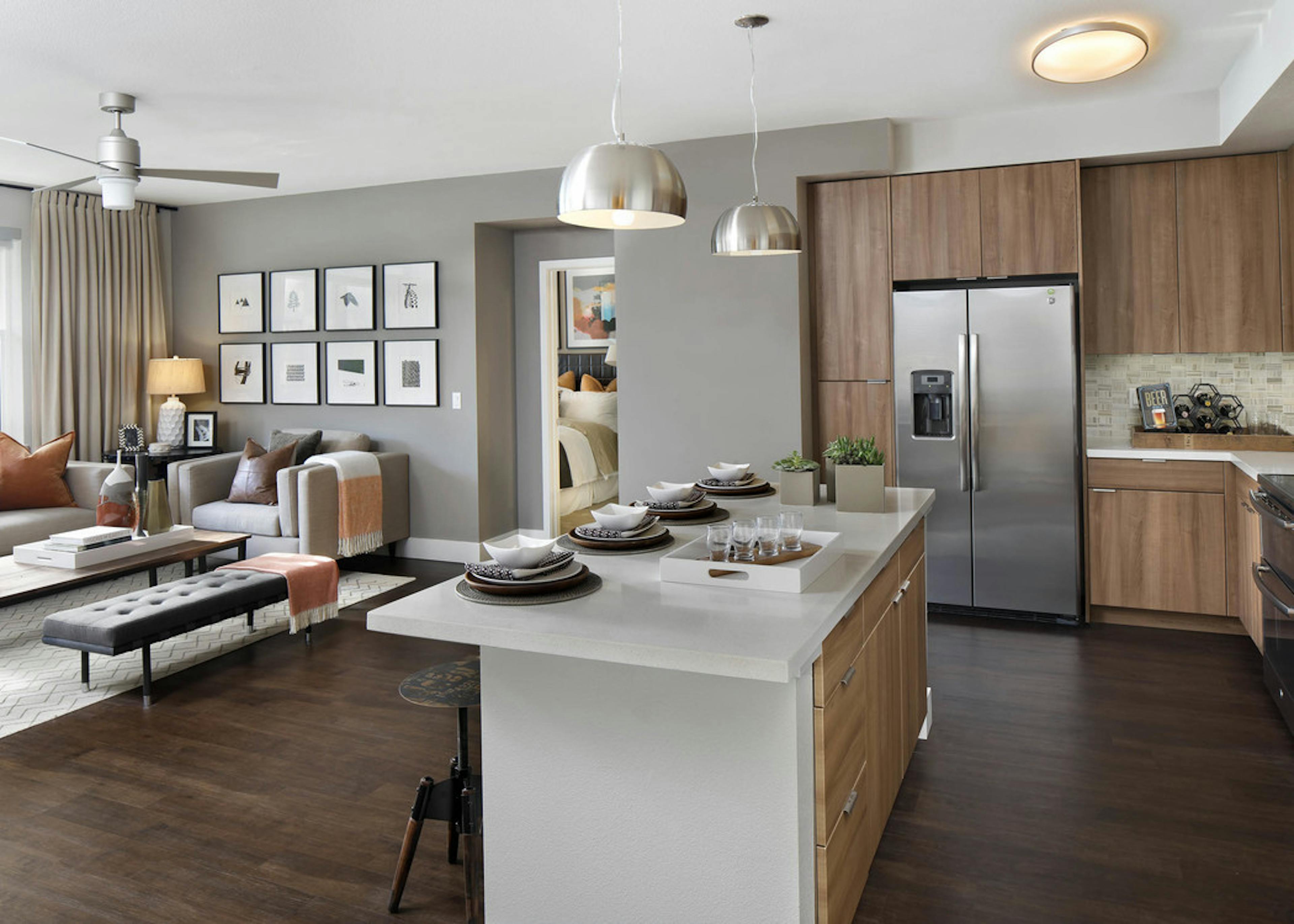 Interior of AMLI Uptown Orange apartment kitchen with quartz counters flowing into a furnished living room with ceiling fan