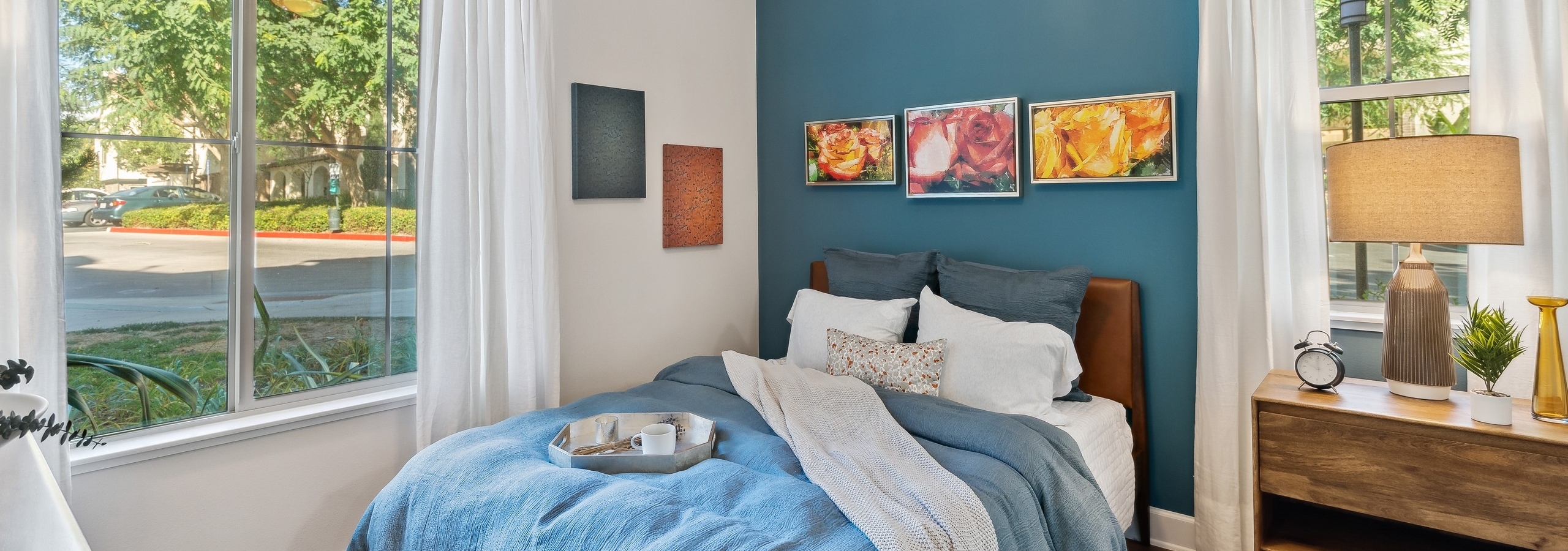 AMLI Spanish Hills bedroom with bed with blue blanket and pillows and hardwood floors and blue accent wall and large windows
