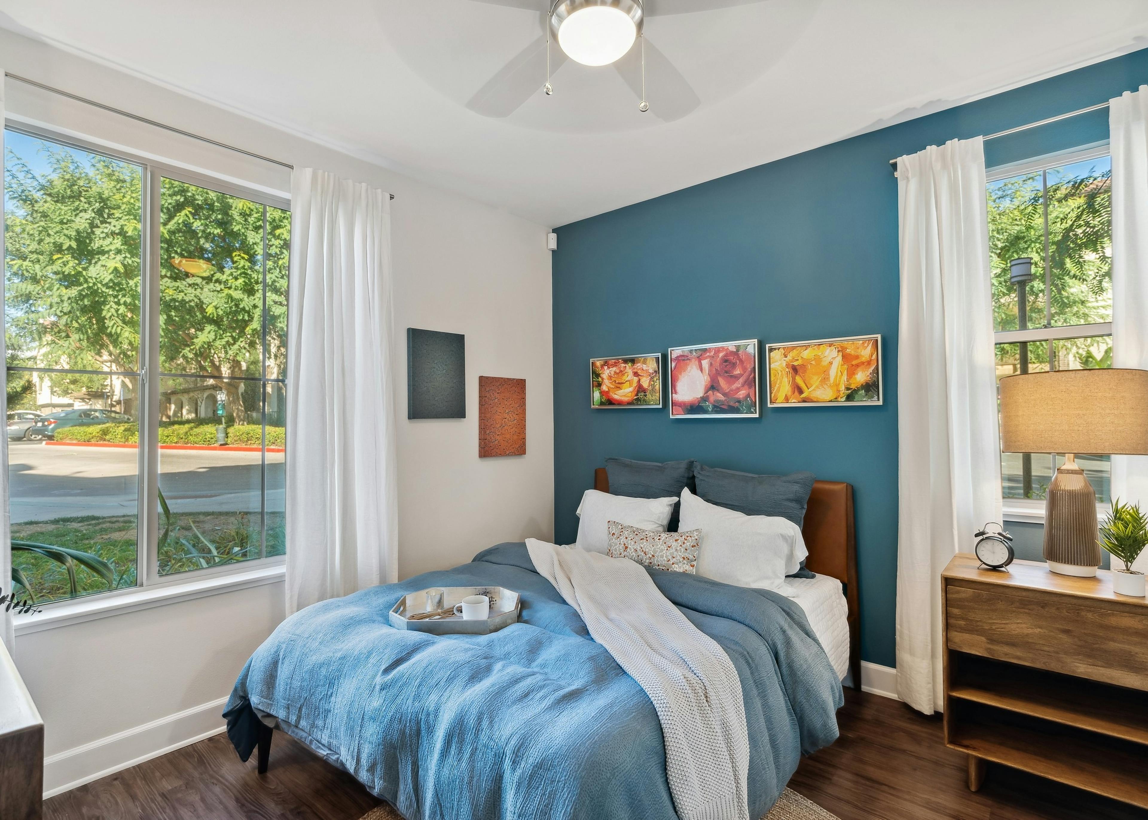 AMLI Spanish Hills bedroom with bed with blue blanket and pillows and hardwood floors and blue accent wall and large windows