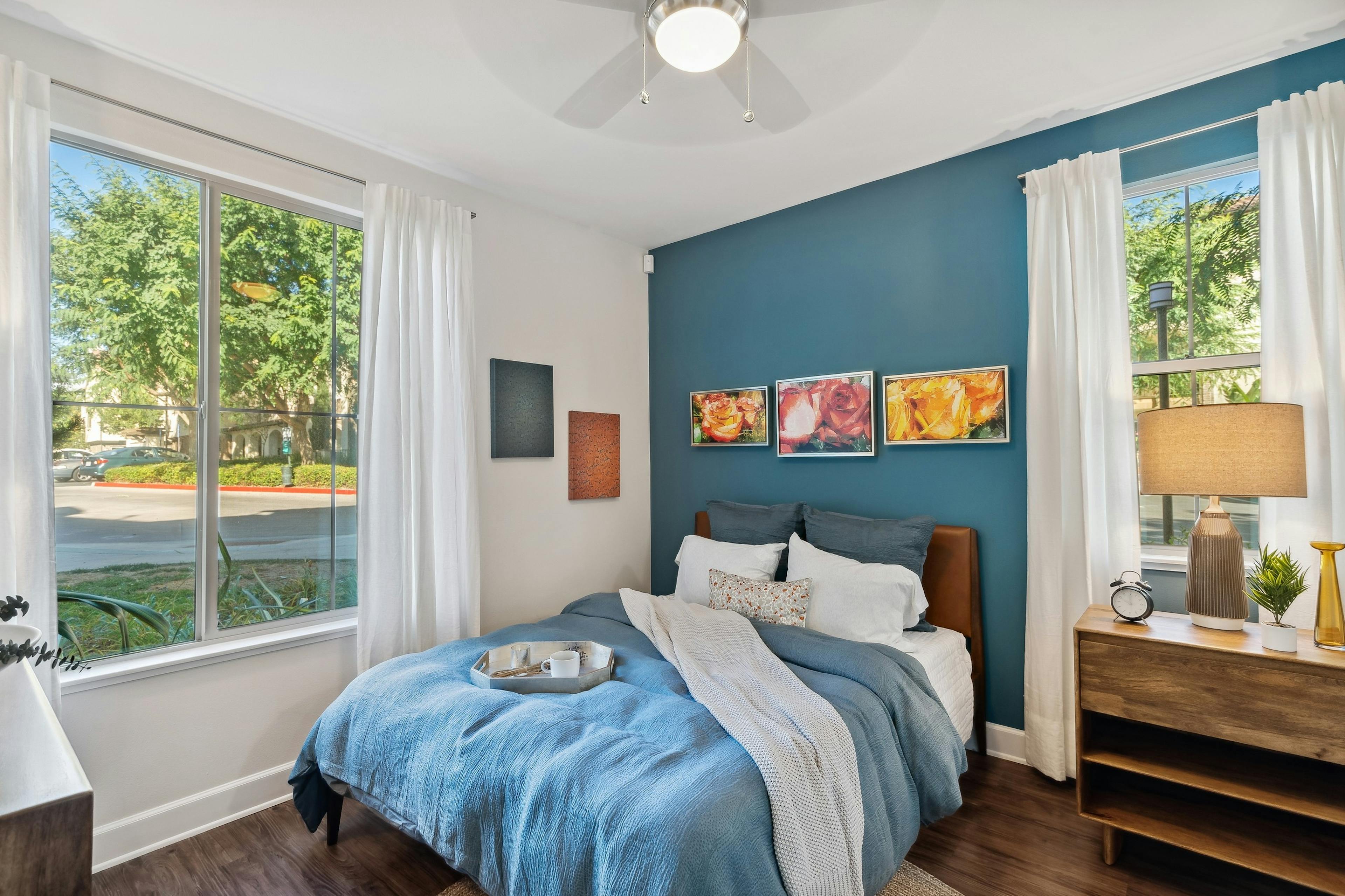 AMLI Spanish Hills bedroom with bed with blue blanket and pillows and hardwood floors and blue accent wall and large windows