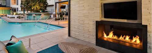 Dusk view of AMLI Uptown Orange outdoor fireplace with individual large screen TV and comfortable seating overlooking pool
