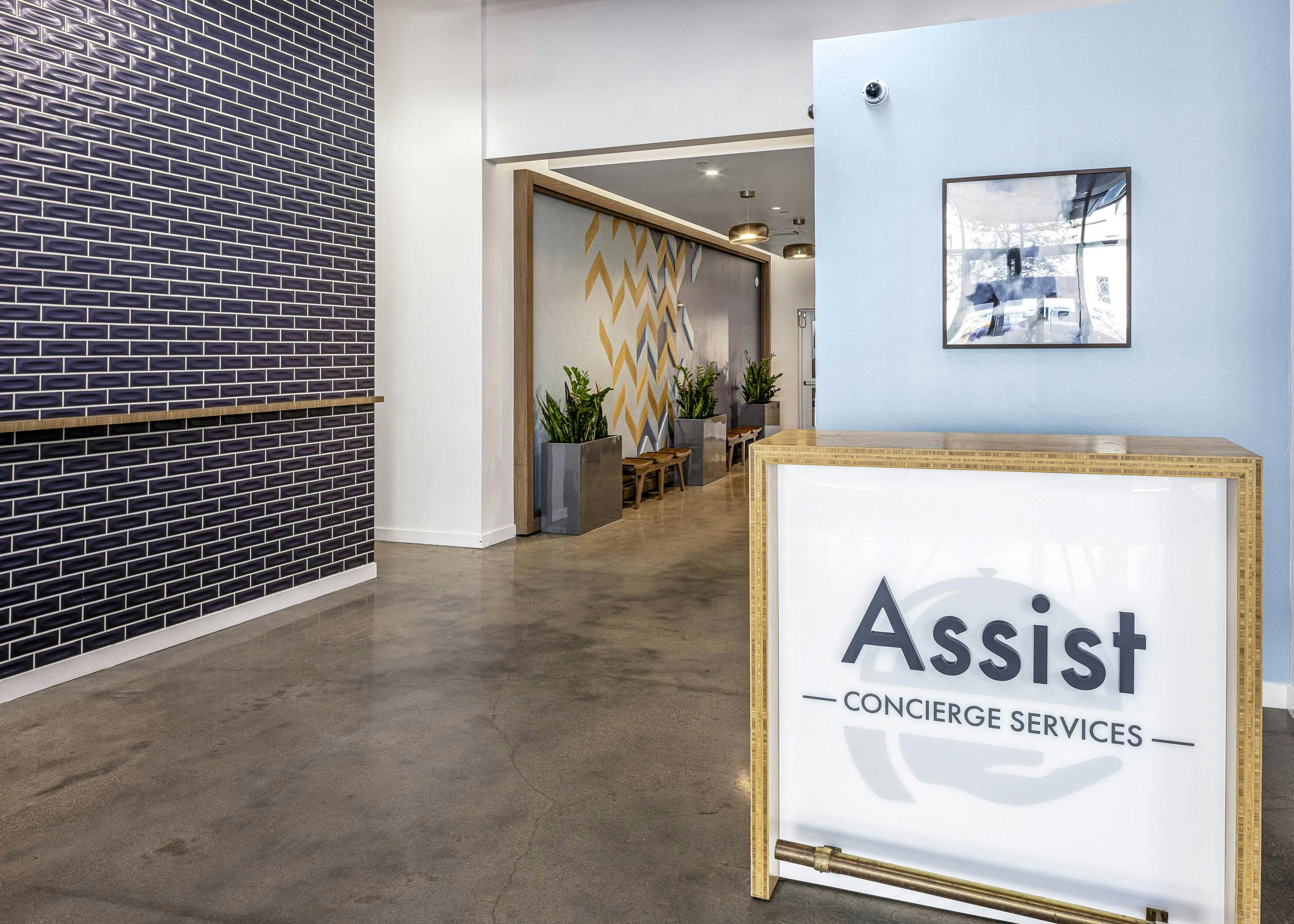 AMLI on 2nd concierge desk with large assist sign in front of light blue wall and across from blue tile wall on concrete floor