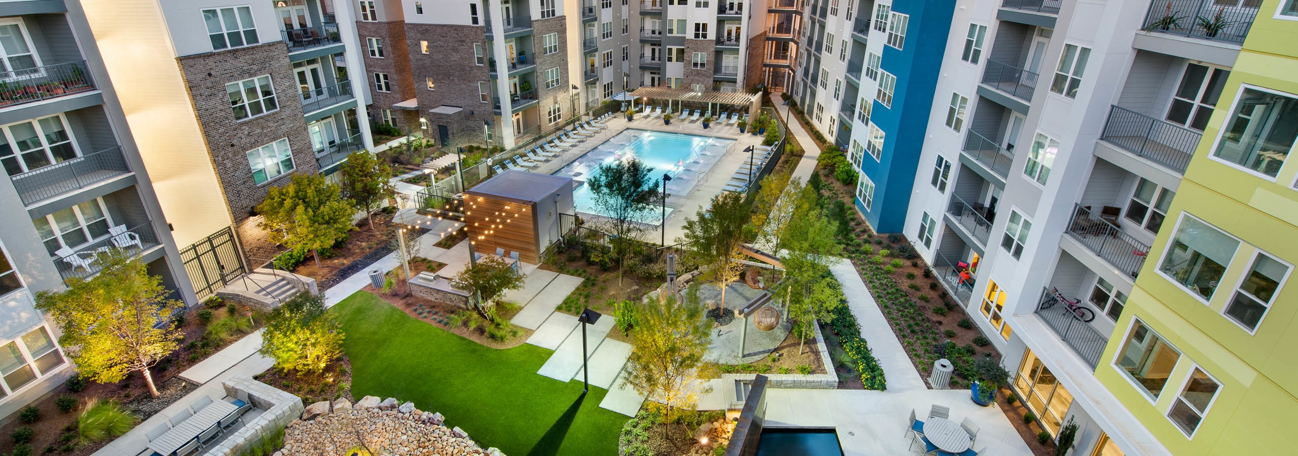 AMLI Piedmont Heights courtyard with large pool and lounge chairs surrounded by lit green areas and foliage at dusk