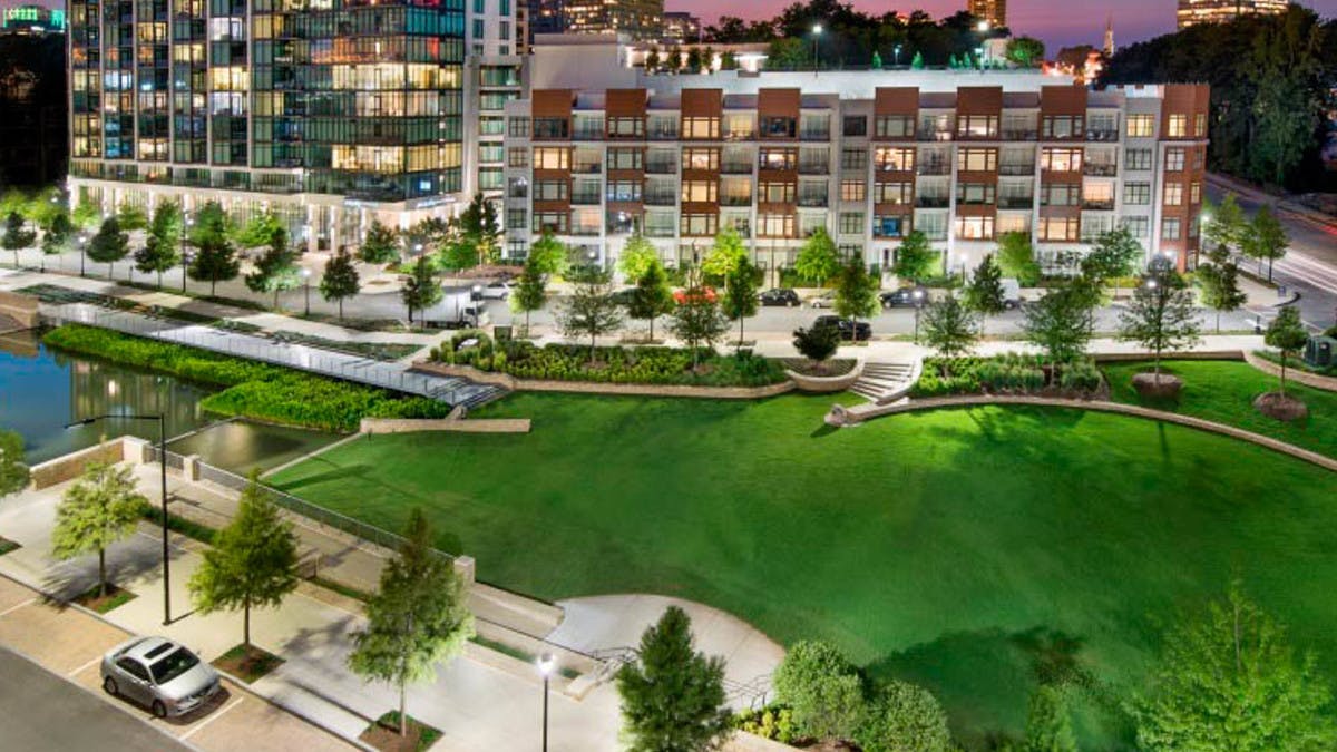 Exterior of the AMLI 3464 building at nighttime with trees and lights lining the pavement and vibrant grass on the other side