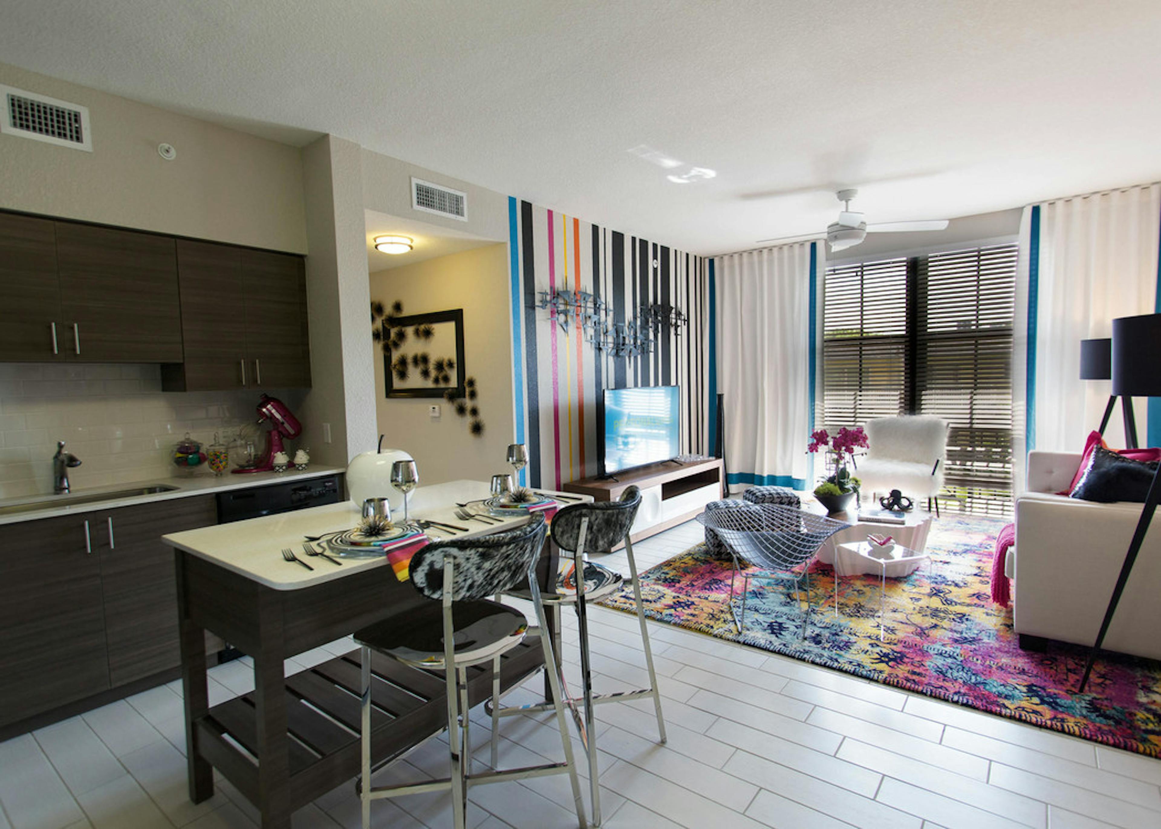 AMLI Dadeland apartment living area with black and white wall, TV on console, hounds tooth stools and a peek into the kitchen
