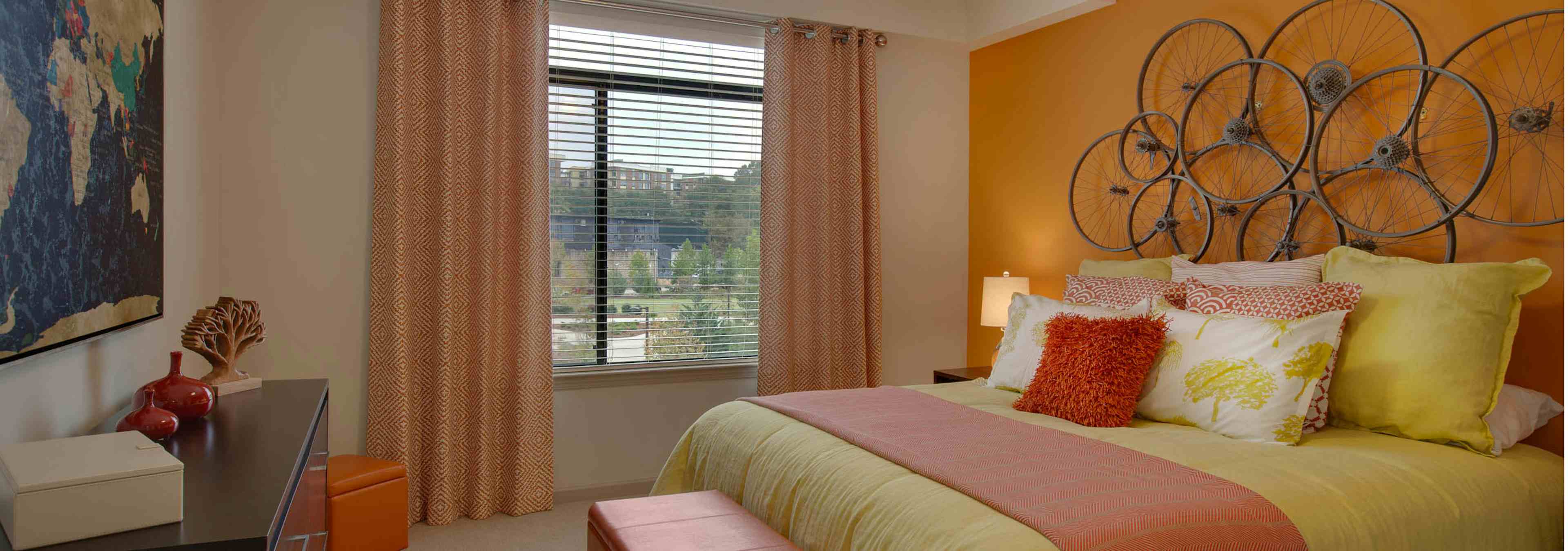 AMLI Ponce Park bedroom with a pink and yellow bed under circular art piece hanging on bright orange wall with a large window