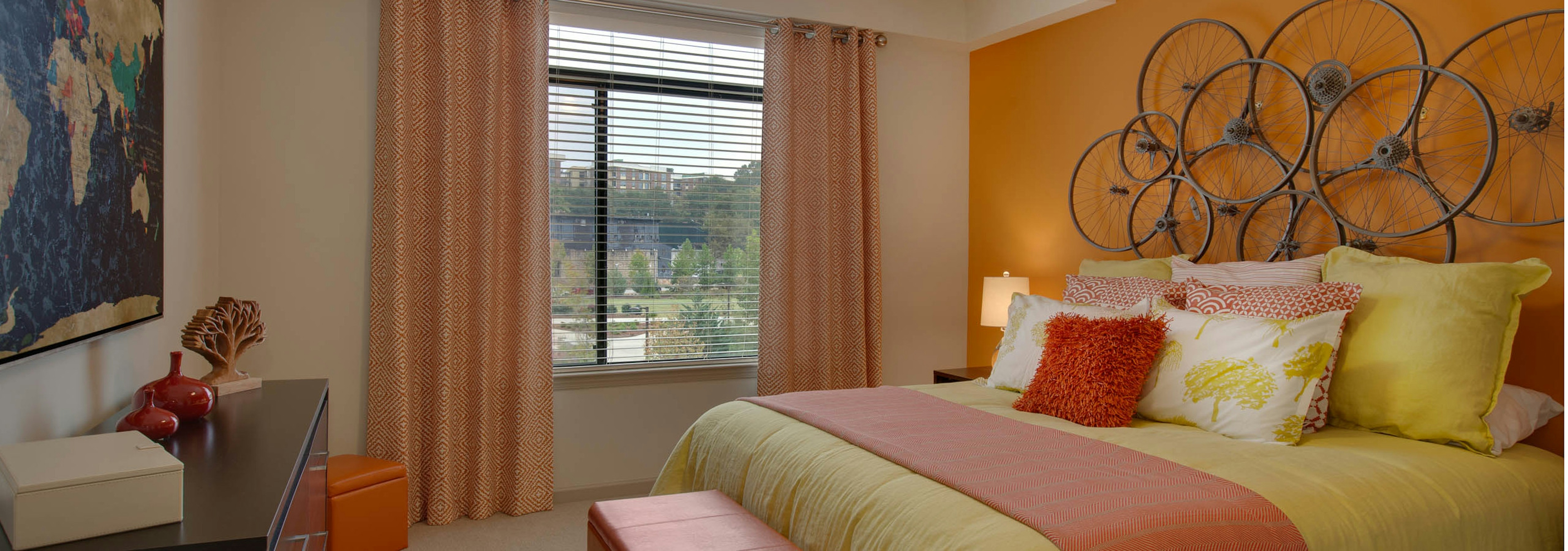 AMLI Ponce Park bedroom with a pink and yellow bed under circular art piece hanging on bright orange wall with a large window