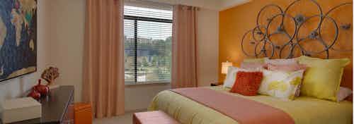 AMLI Ponce Park bedroom with a pink and yellow bed under circular art piece hanging on bright orange wall with a large window
