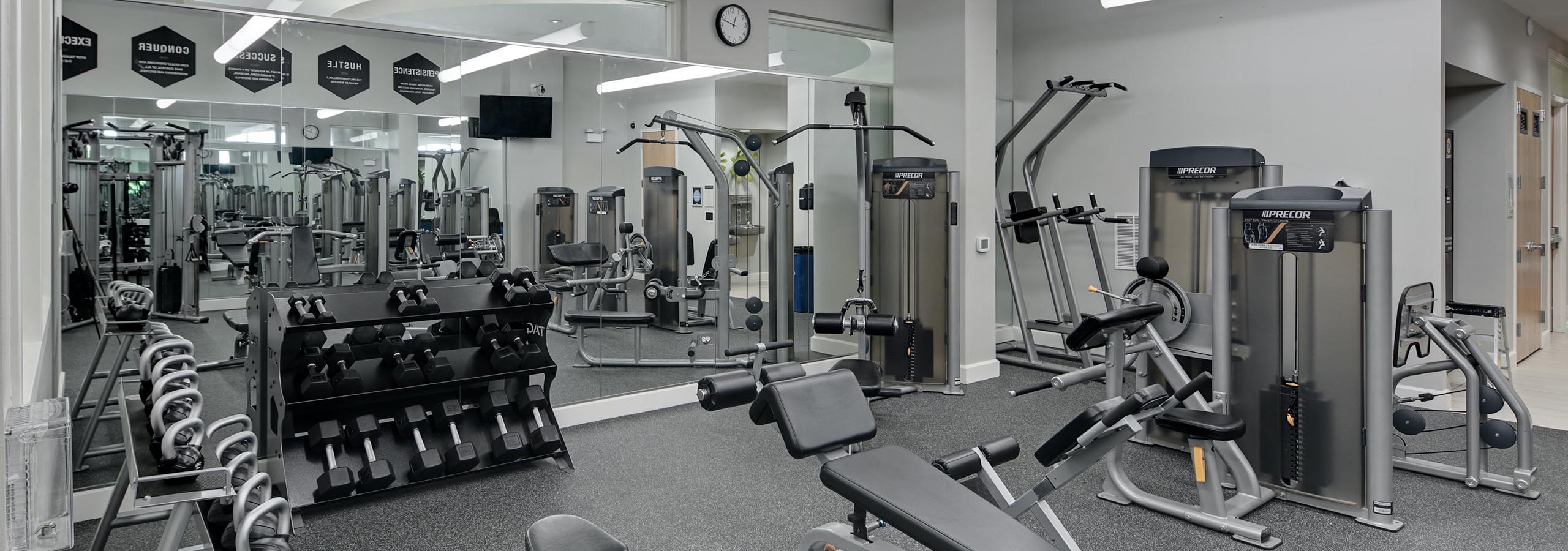 Weight benches in the AMLI Evanston fitness center surrounded by kettlebell and dumbbell weight racks facing large wall mirror