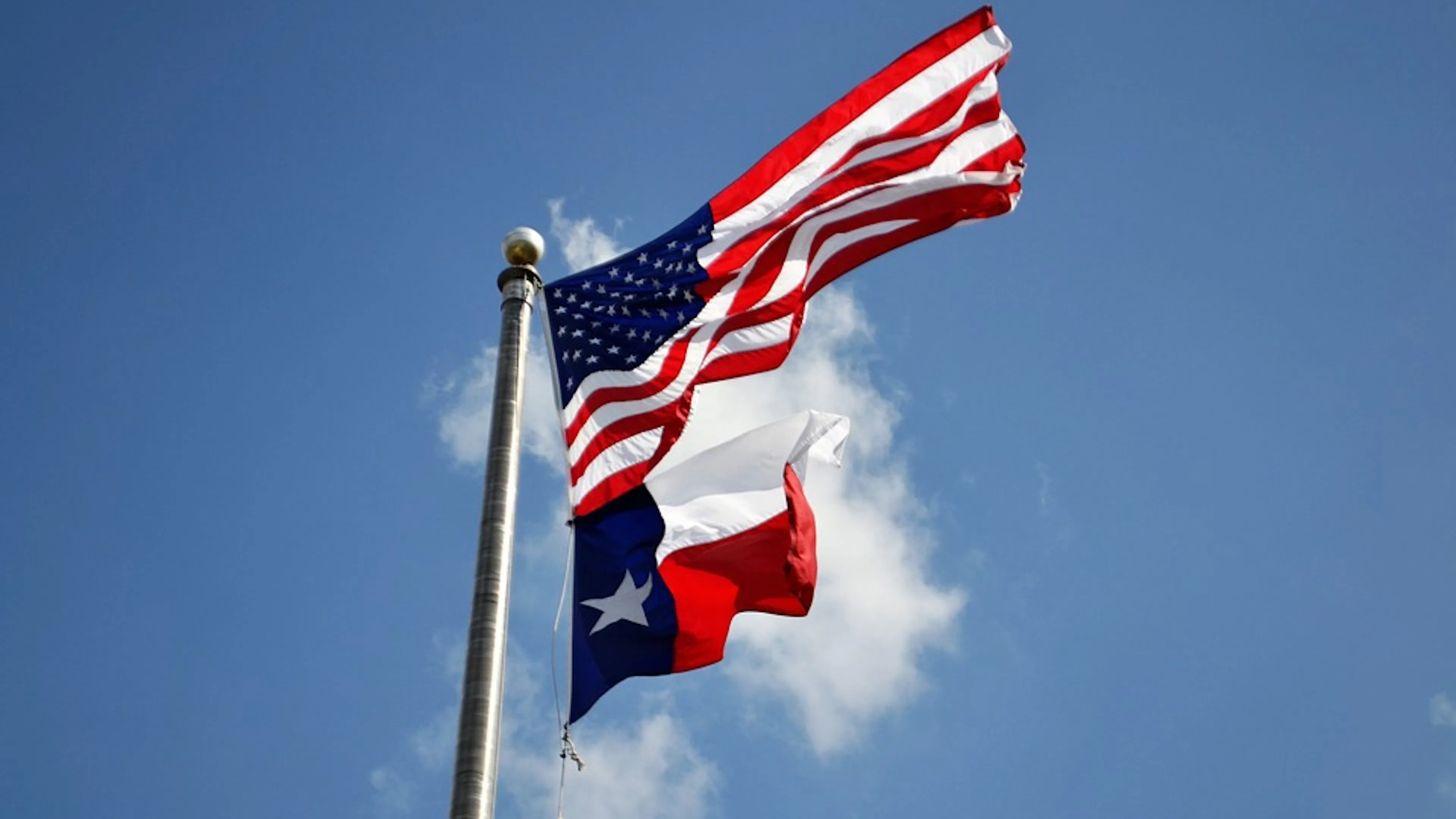 The American flag and the Texas state flag flying in the wind with the blue sky in the background