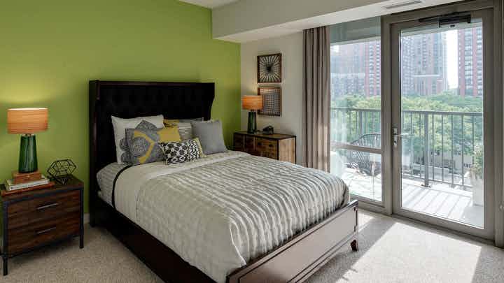 Furnished bedroom with lime green wall and queen sized bed at AMLI 900 with floor to ceiling windows and private balcony.