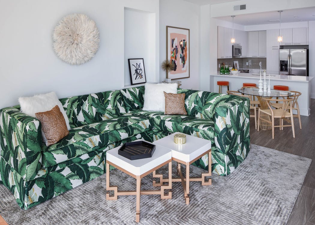 Alternate view of AMLI 3464 living room with palm branch sofa and the kitchen with a counter and barstools in the background