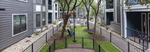 Large courtyard at AMLI Eastside apartments during the day with a fenced dog park with green turf and Adirondack chairs