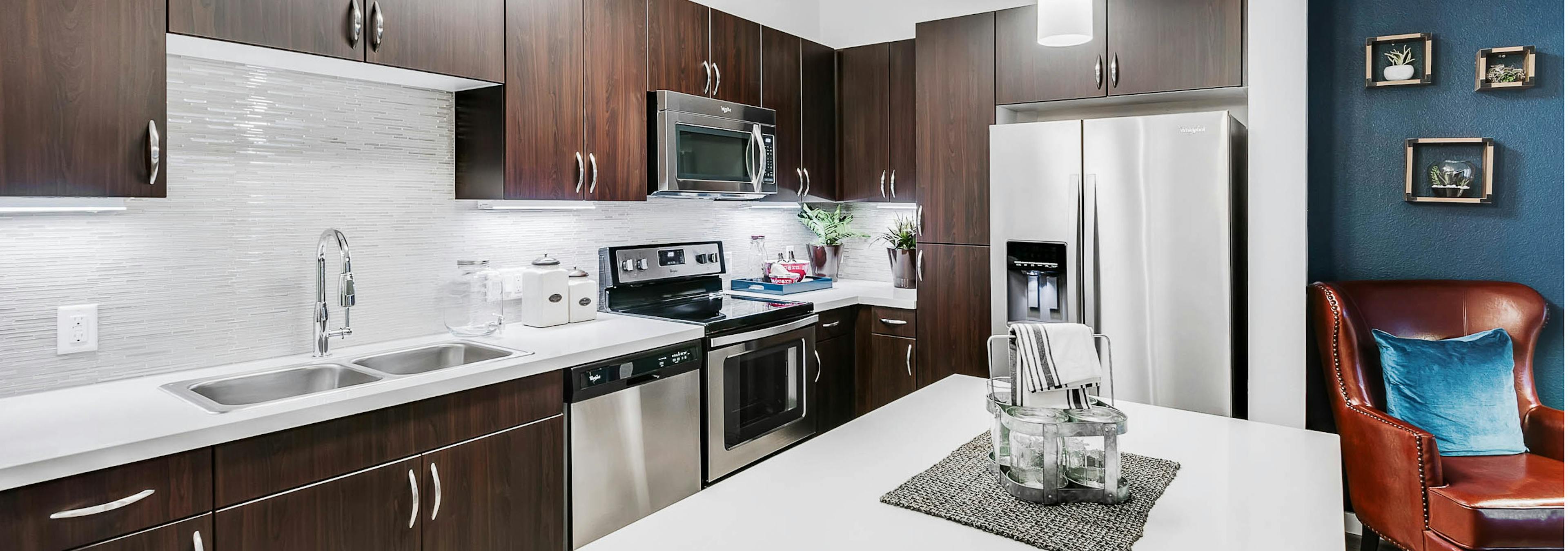 Interior view of a kitchen at AMLI Cherry Creek apartments with an island and white granite counter top and living room chair