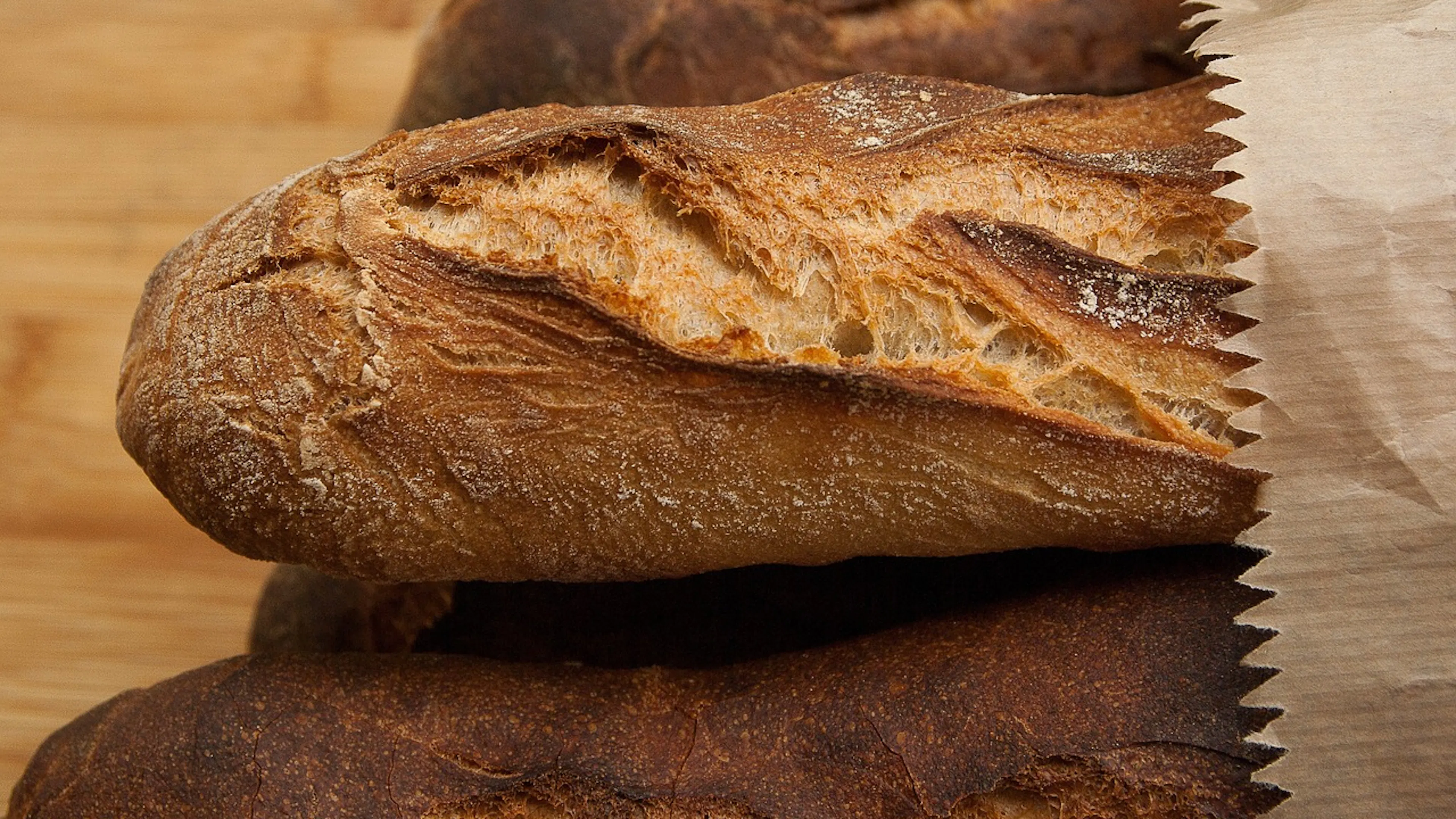 A brown paper bag resting on its side with four fresh baguettes sticking out from the top
