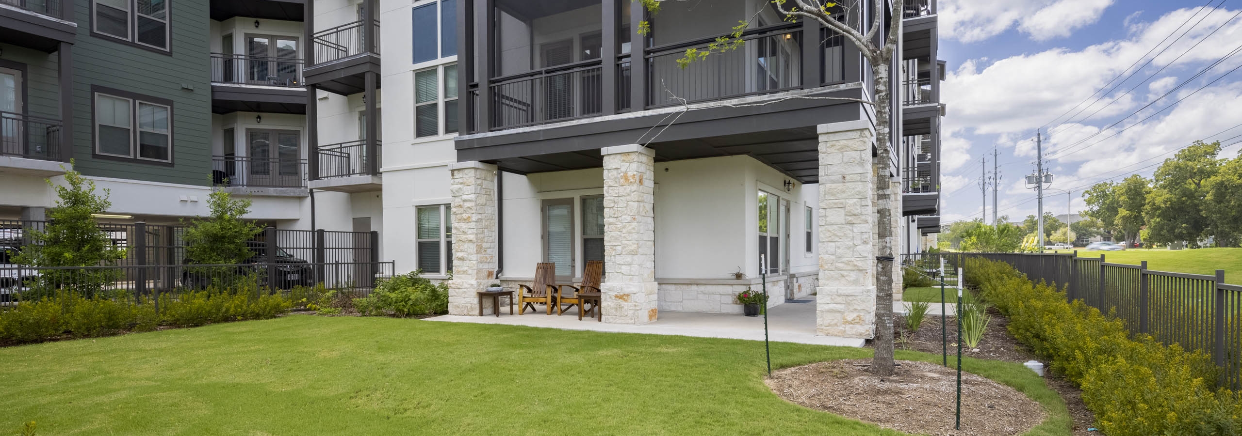 Daytime view of AMLI Lakeline apartment oversized outdoor patio featuring a large grass lawn and lush surrounding landscaping