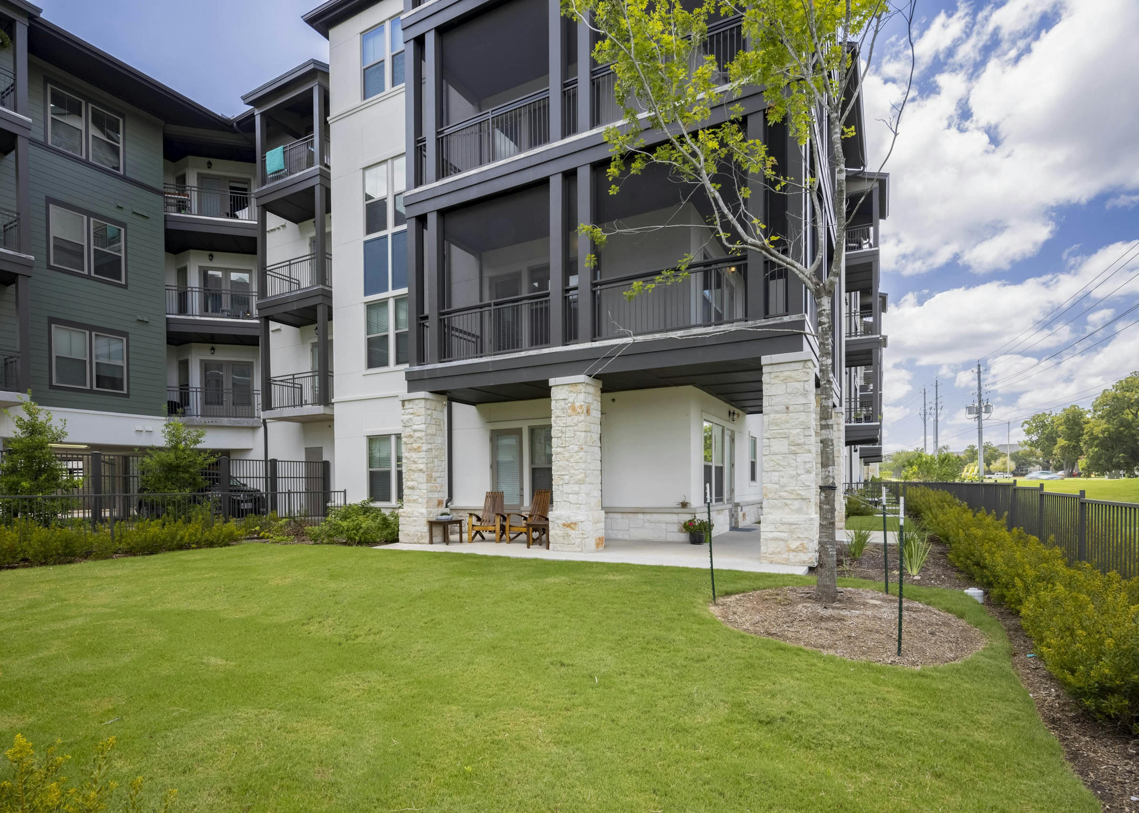 Daytime view of AMLI Lakeline apartment oversized outdoor patio featuring a large grass lawn and lush surrounding landscaping