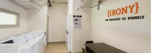 Interior of laundry room at AMLI at Mueller with washer and dryer machines and a wall stencil reading IRONY above a table