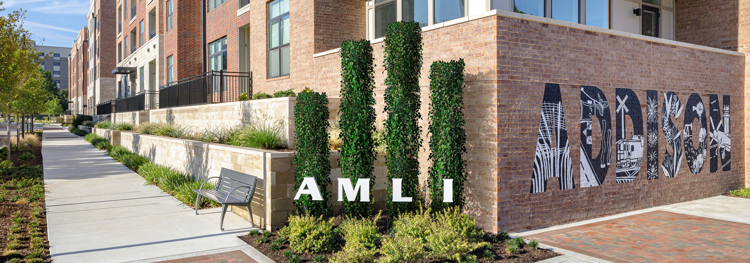 AMLI Addison orange brick building with four pristinely landscaped shrubs with letters spelling AMLI next to a wall mural