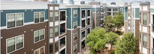 Exterior view of AMLI Eastside apartment community courtyard with view of building facade and vibrant foliage on a sunny day