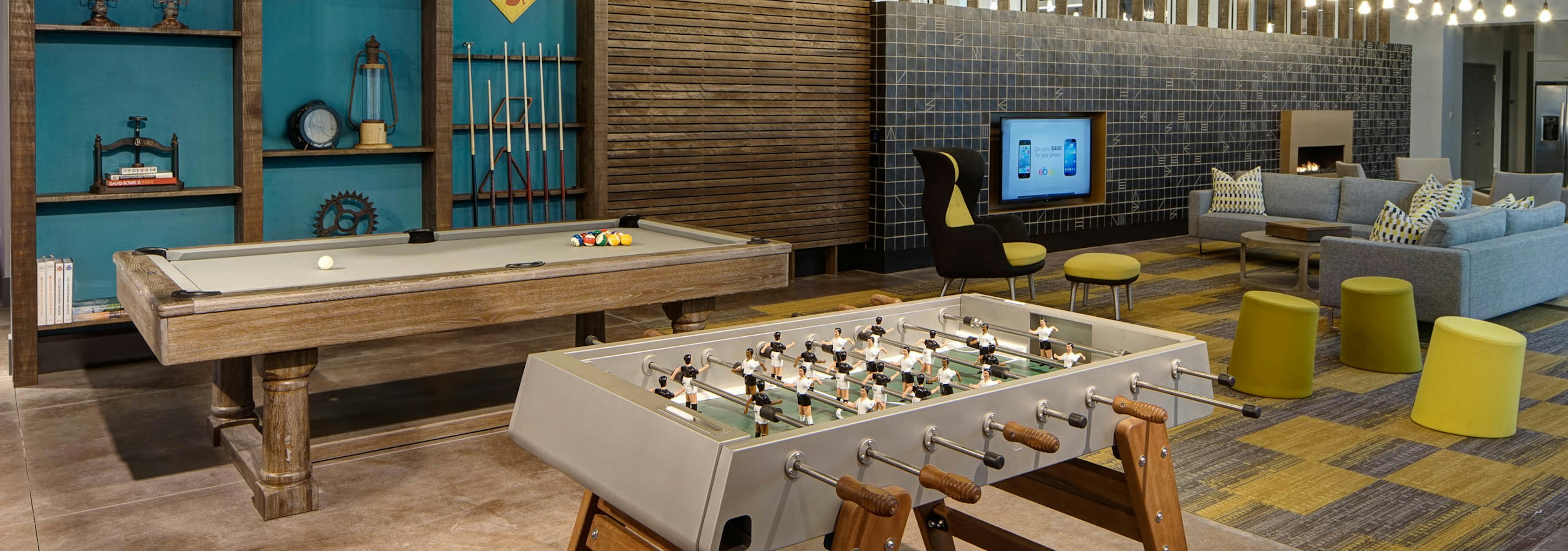 Modern clubroom at AMLI Lofts with billiard and foosball tables and a seating area with a large TV in the background