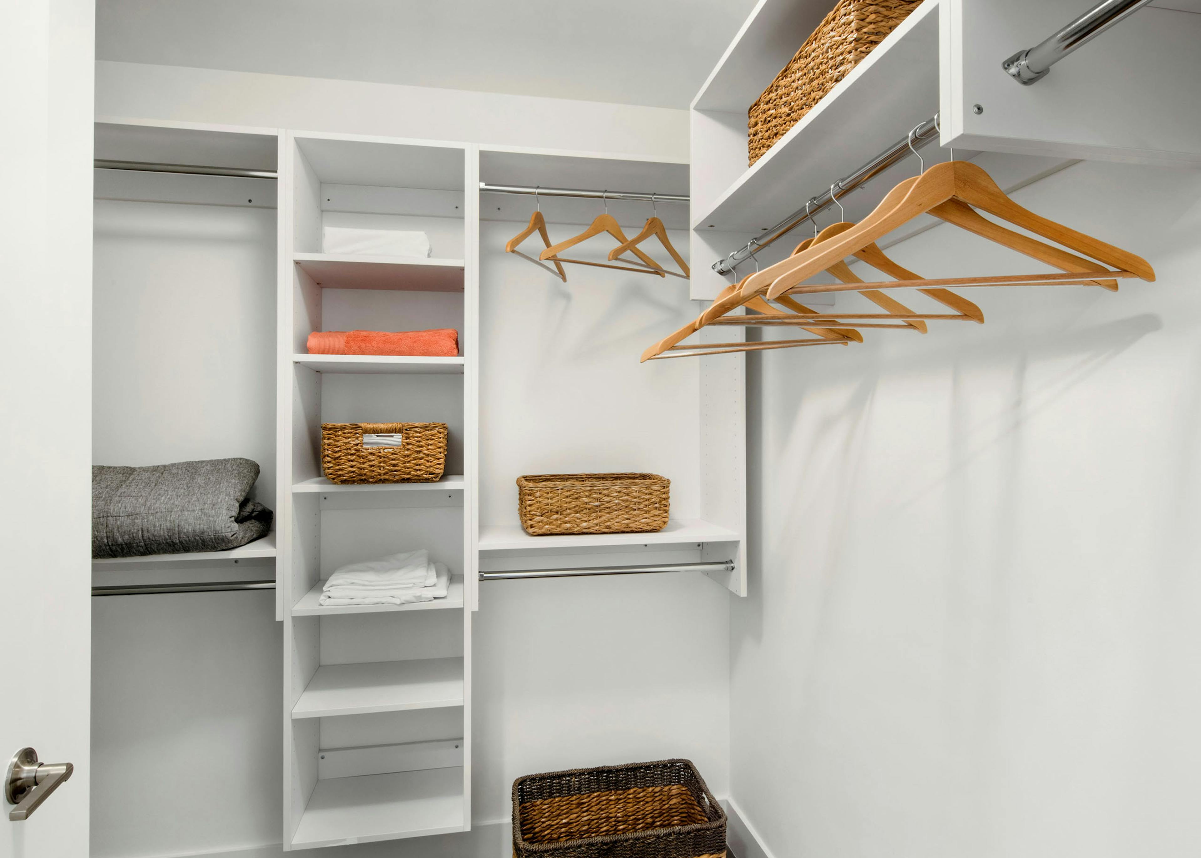Walk in closet at AMLI Midtown 29 apartments with white hanging shelves and wooden hangers and wicker baskets