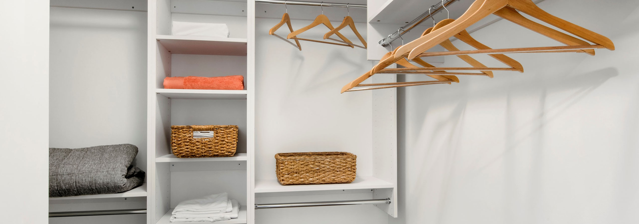 Walk in closet at AMLI Midtown 29 apartments with white hanging shelves and wooden hangers and wicker baskets