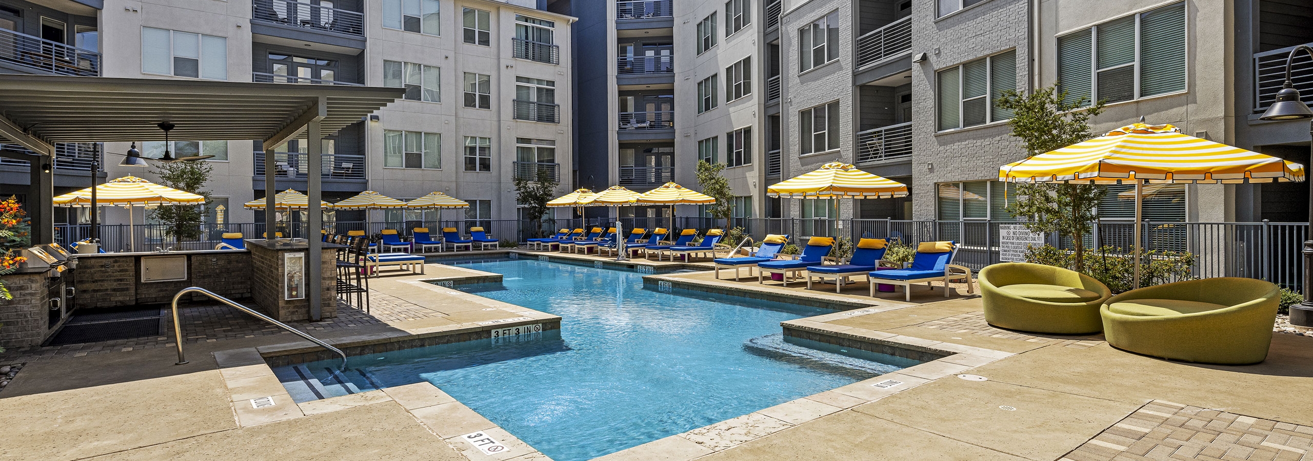AMLI South Shore swimming pool with blue lounge chairs and yellow and white umbrellas in front of gray buildings