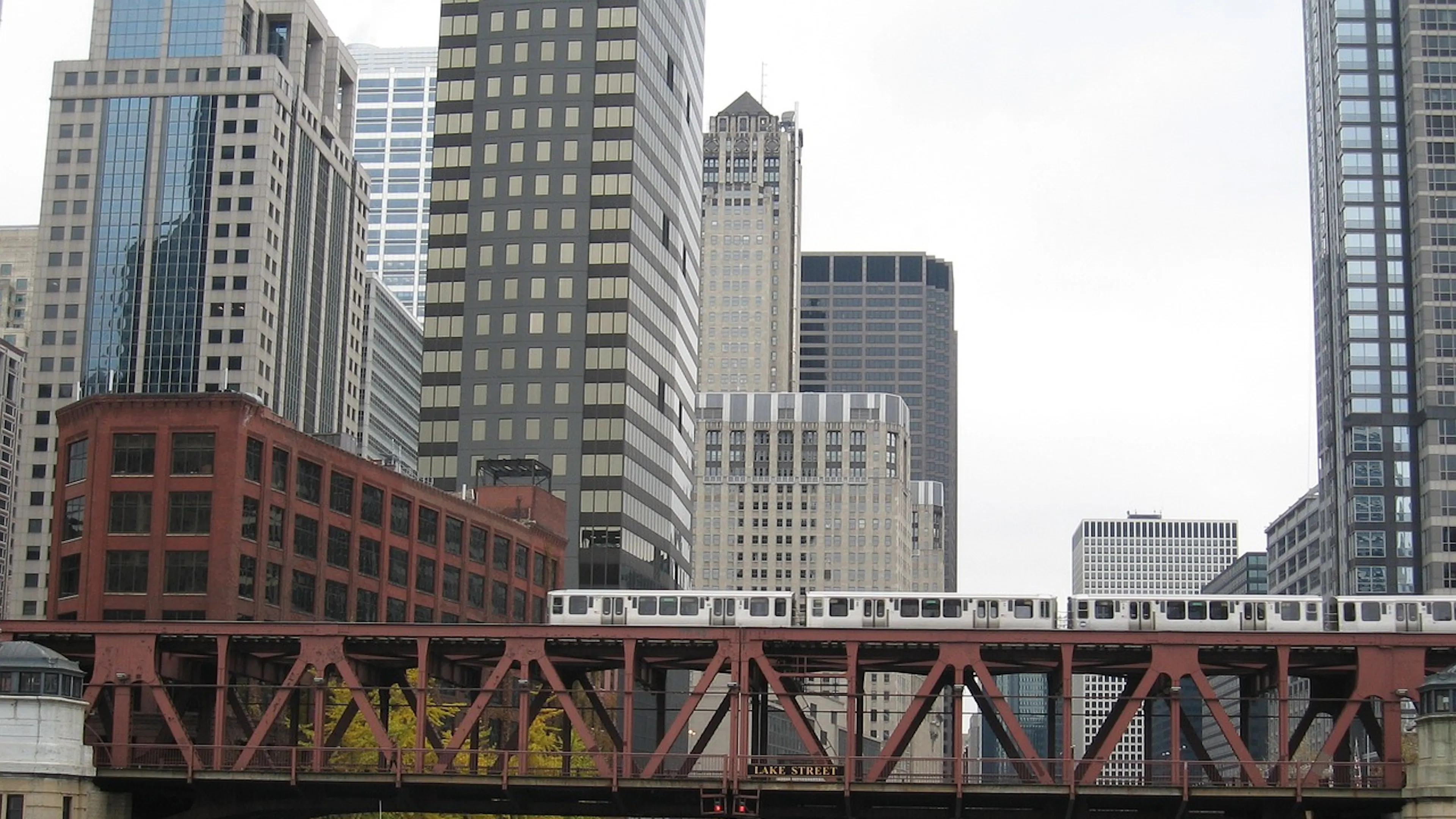 A metal bridge going over the Chicago River in Downtown with a boat passing underneath and a train passing overhead