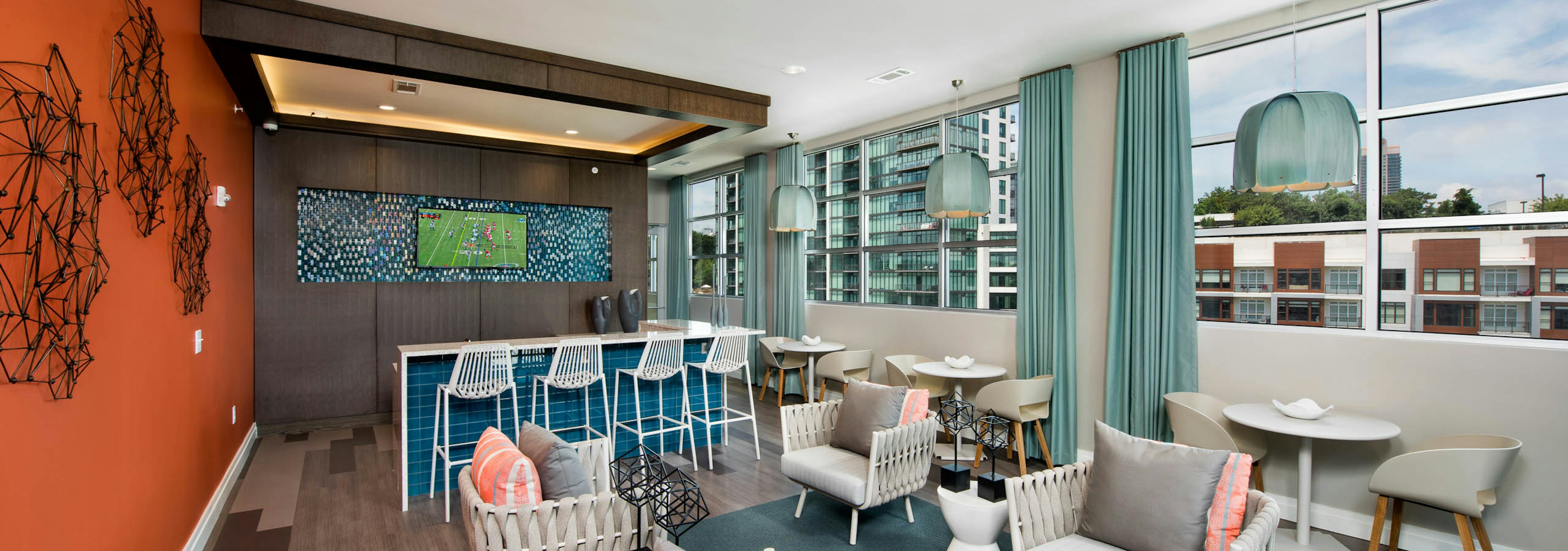 Resident lounge at AMLI Buckhead with an orange accent wall and various seating options near windows with a daytime view